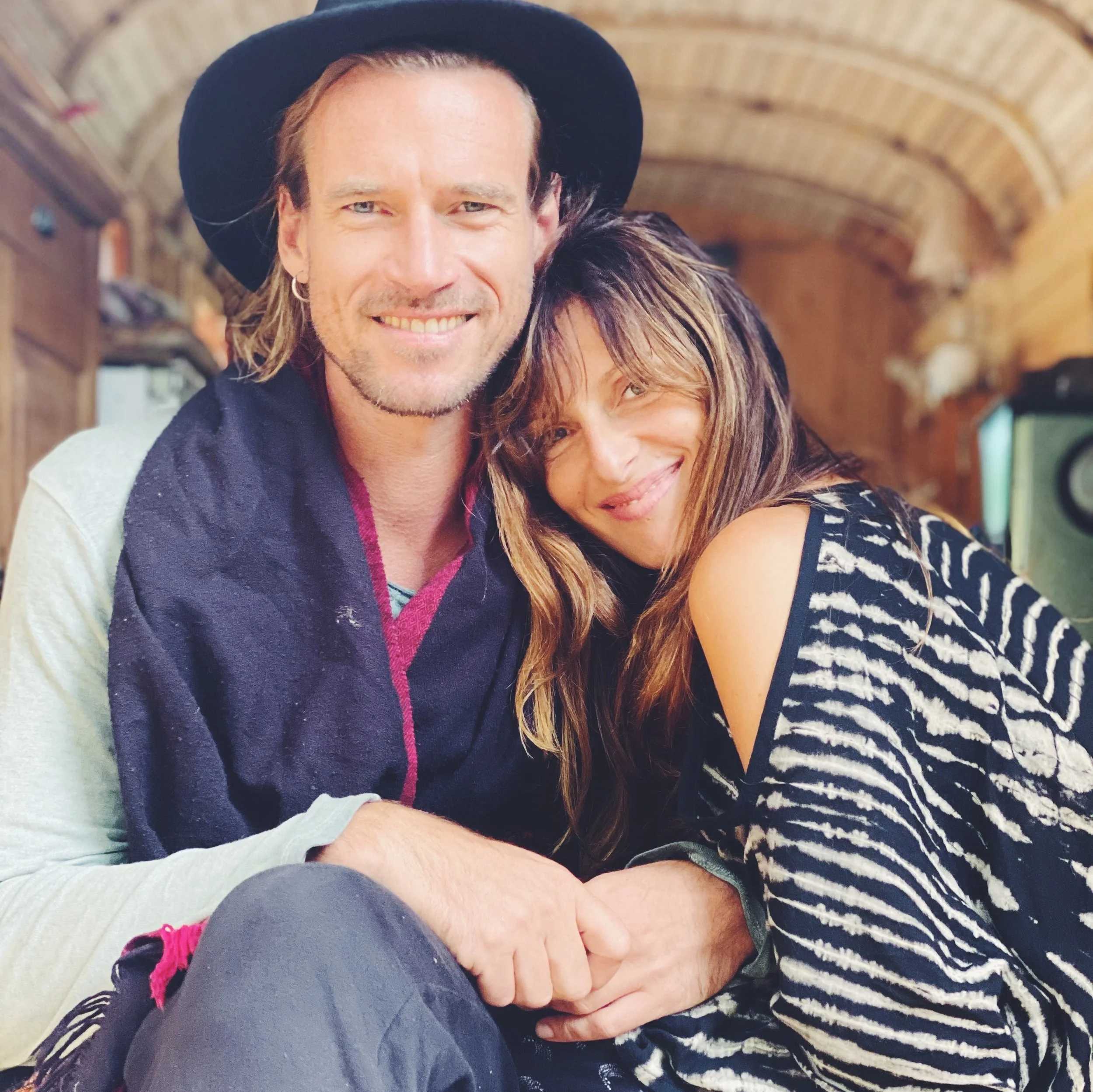A smiling man and woman hugging each other in a cozy wooden room.