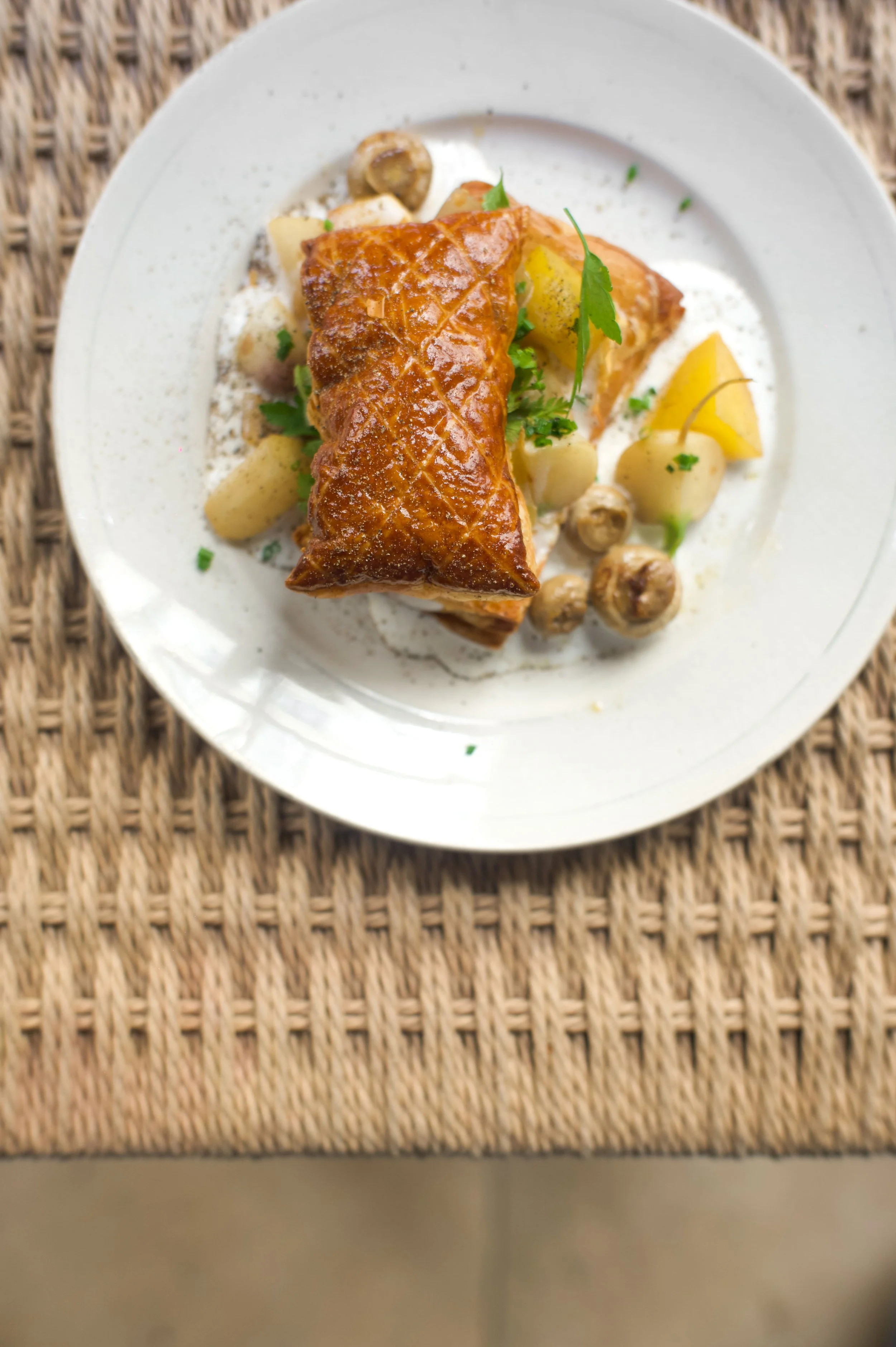 Filet de poisson pané avec pommes de terre et champignons, servi avec des herbes fraîches sur une assiette blanche.