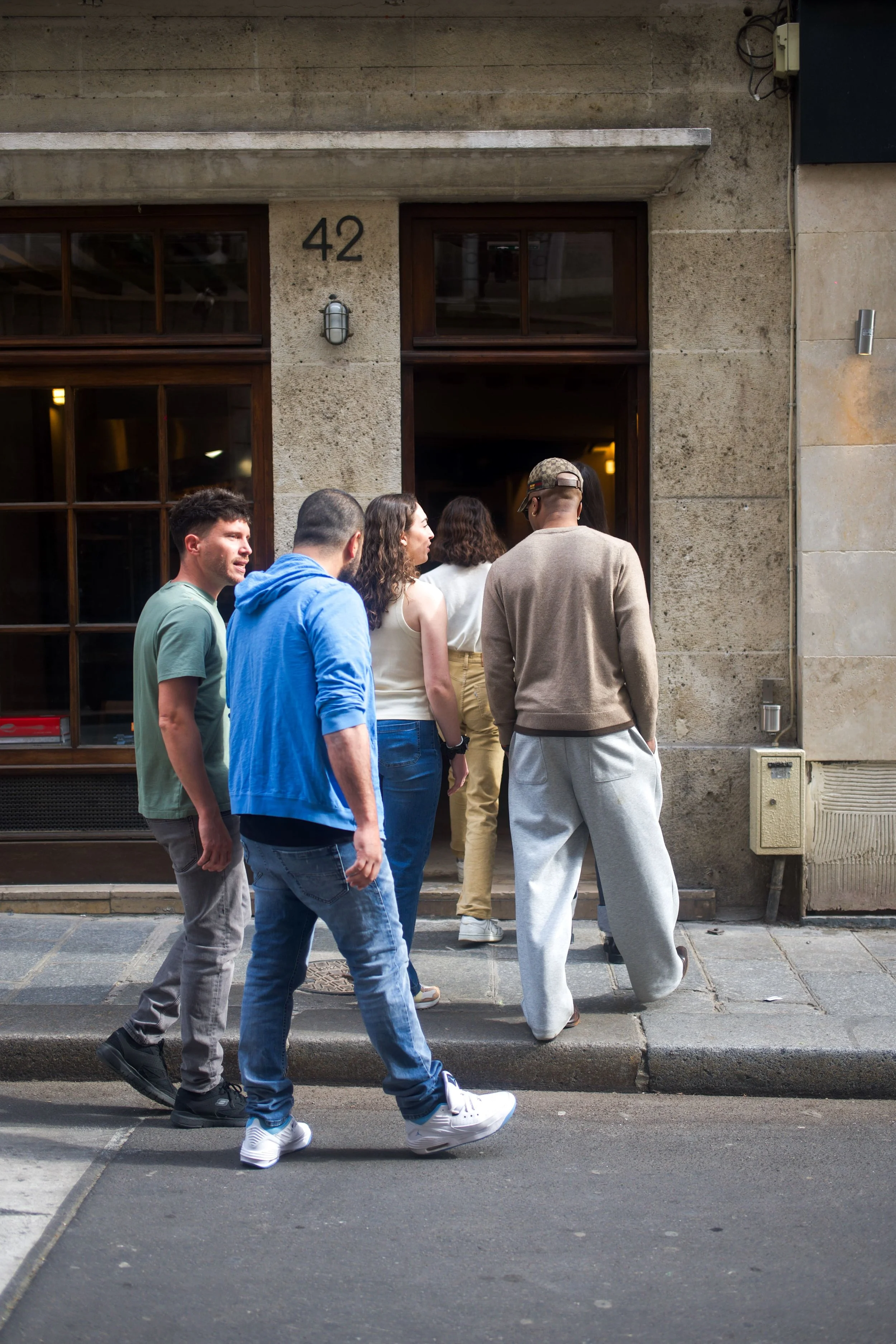 Groupe de personnes faisant la queue devant une porte d'entrée d'un bâtiment en pierre, avec le numéro 42, dans une rue urbaine.