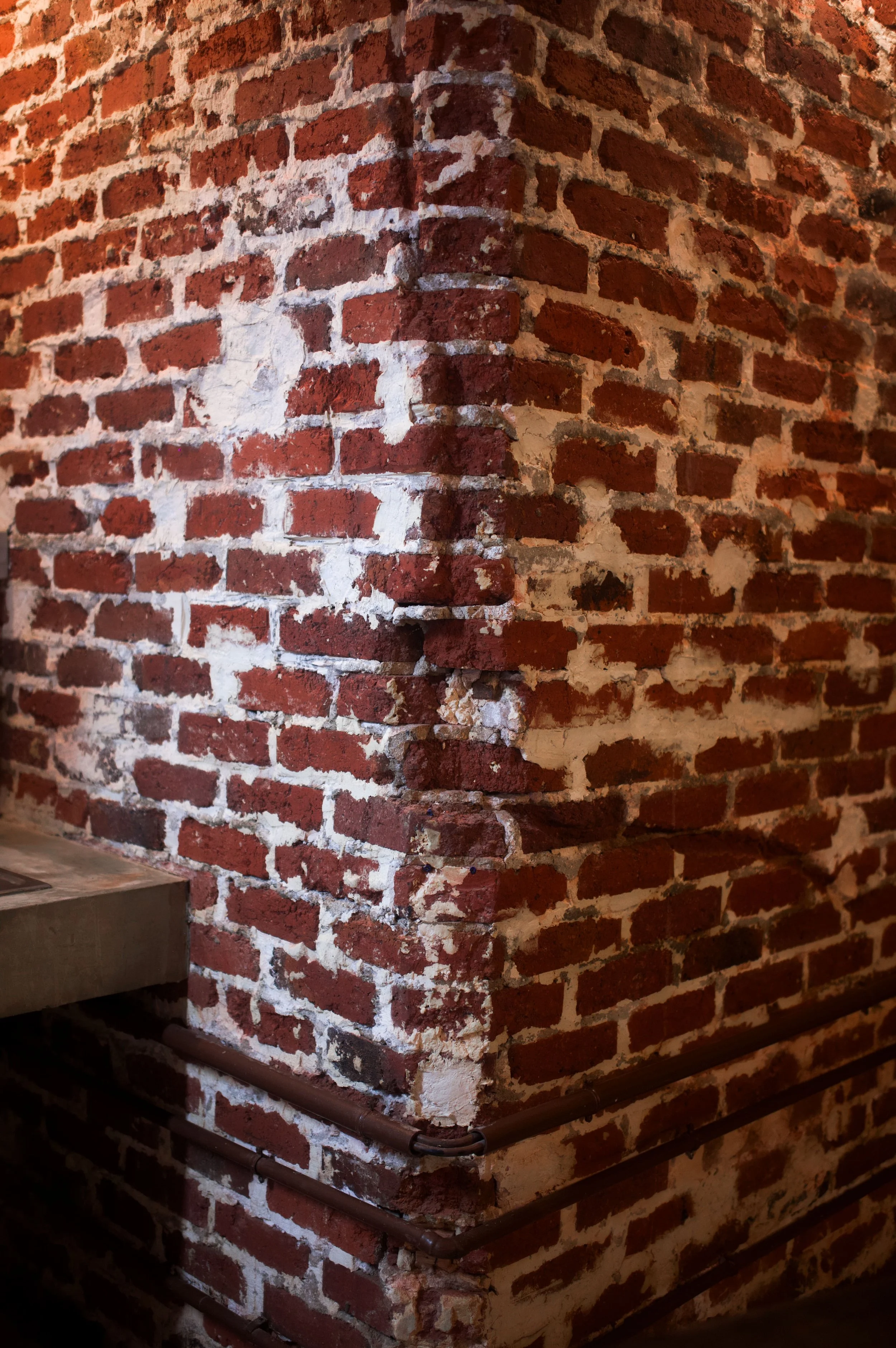 Red brick walls with white joint, corner of a wall with electrical pipes and a wooden shelf.