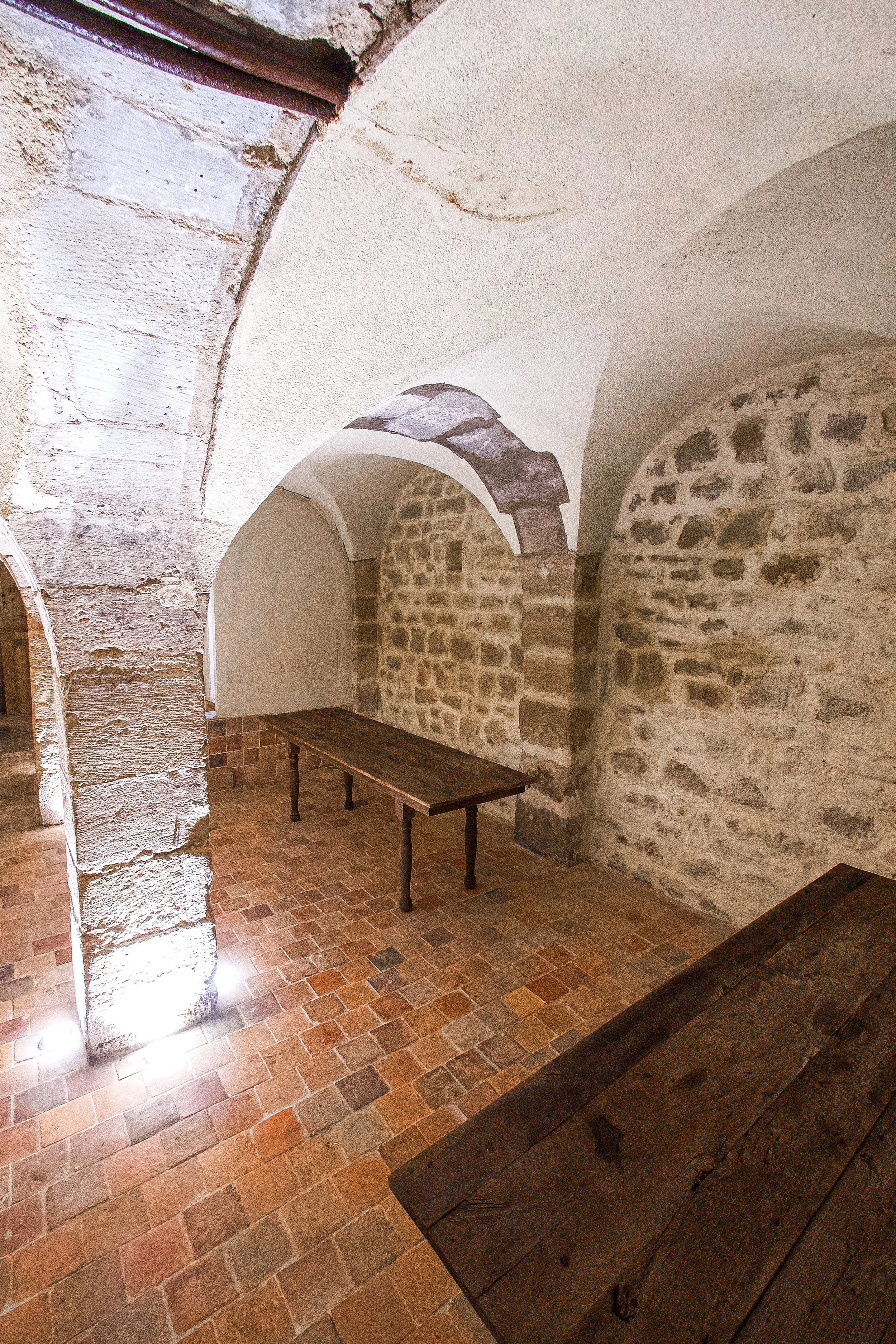 Room with stone walls, vaulted stone ceiling, two wooden tables, terracotta tile floor.