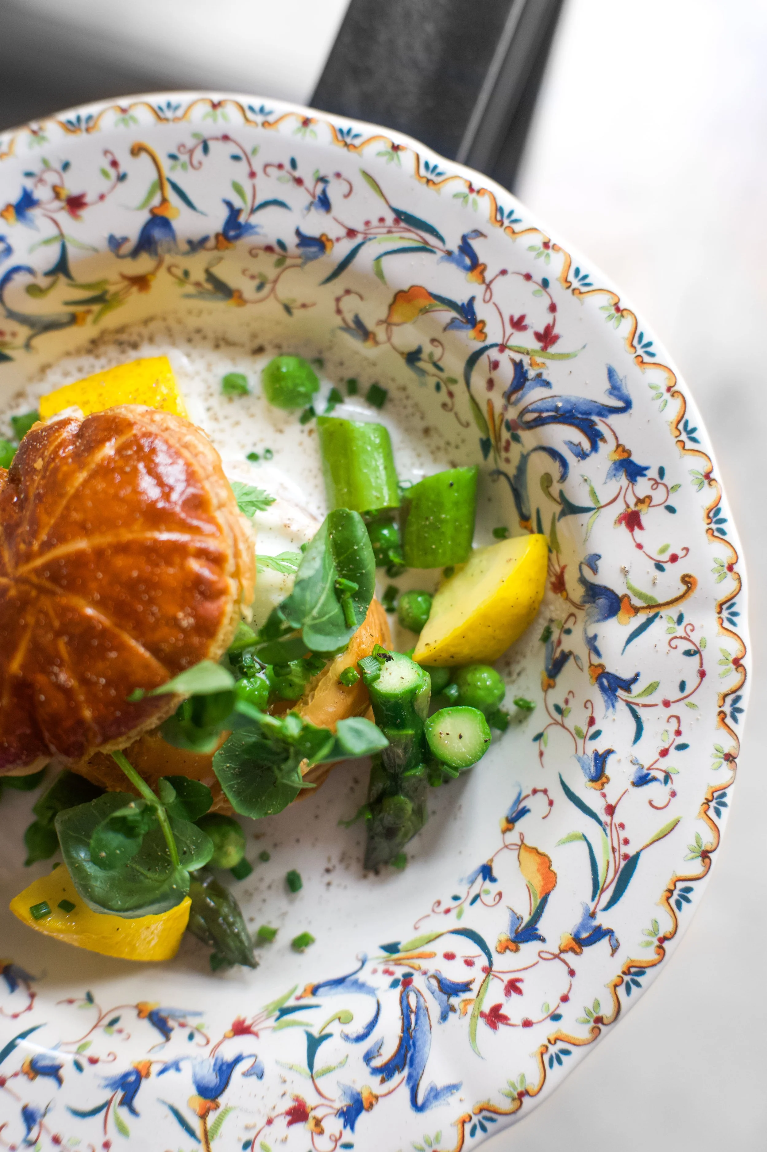 Assiette avec des légumes verts, un œuf mollet dans une coquille, avec un décor floral coloré sur le rebord du plat.