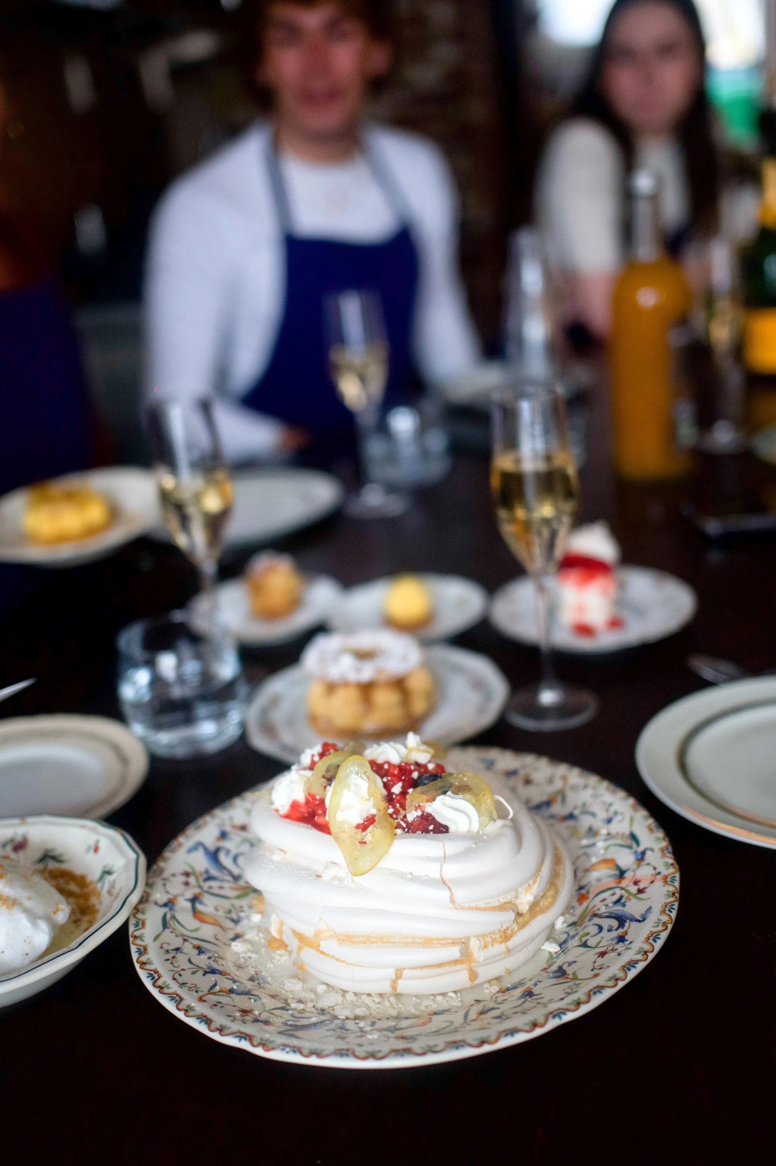 Gâteaux et desserts sur une table, avec deux personnes floues en arrière-plan, lors d'une célébration ou d'un repas festif.
