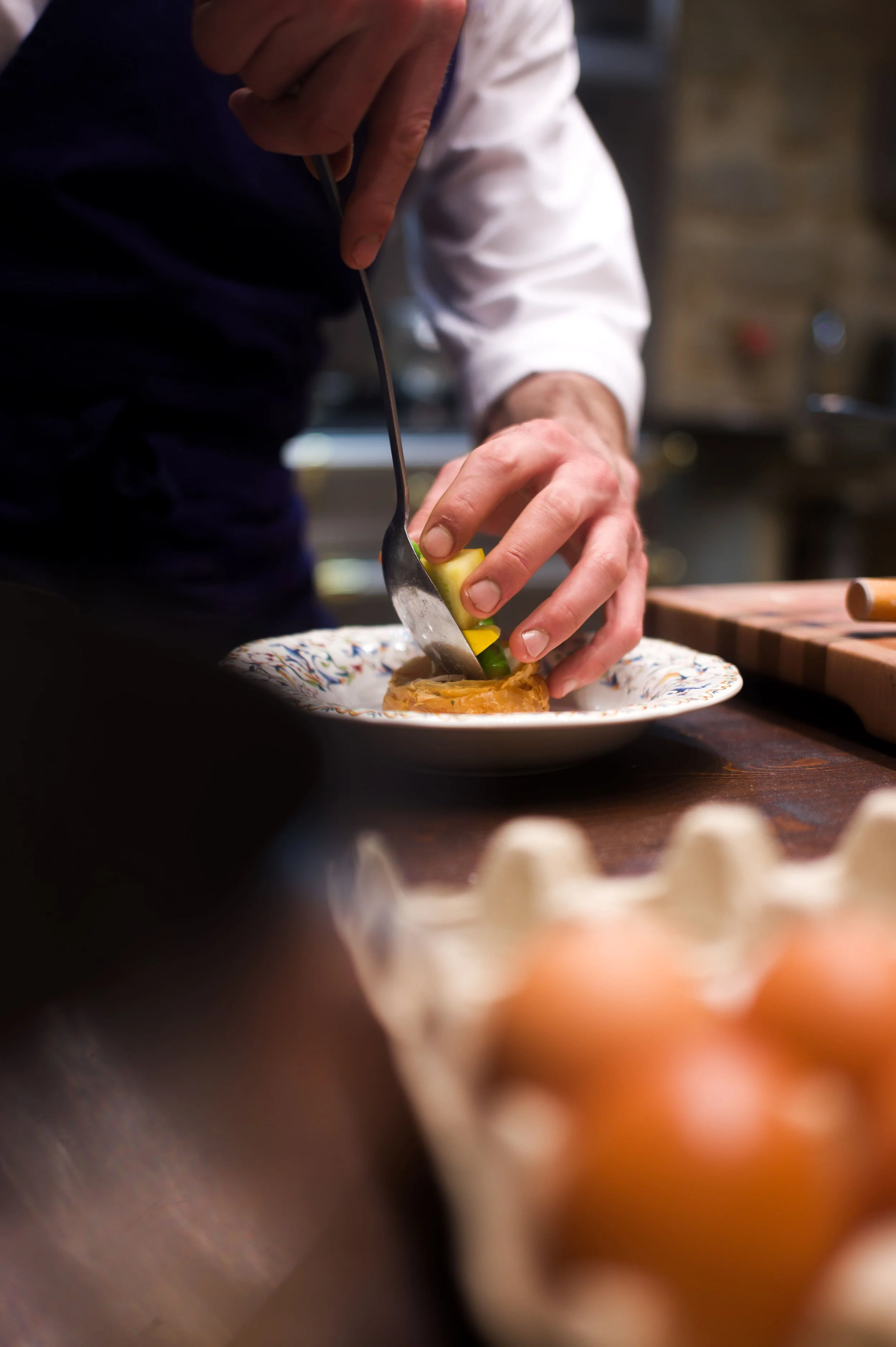 Un chef prépare un plat en utilisant un couteau et une cuillère, avec des œufs de poule à proximité.