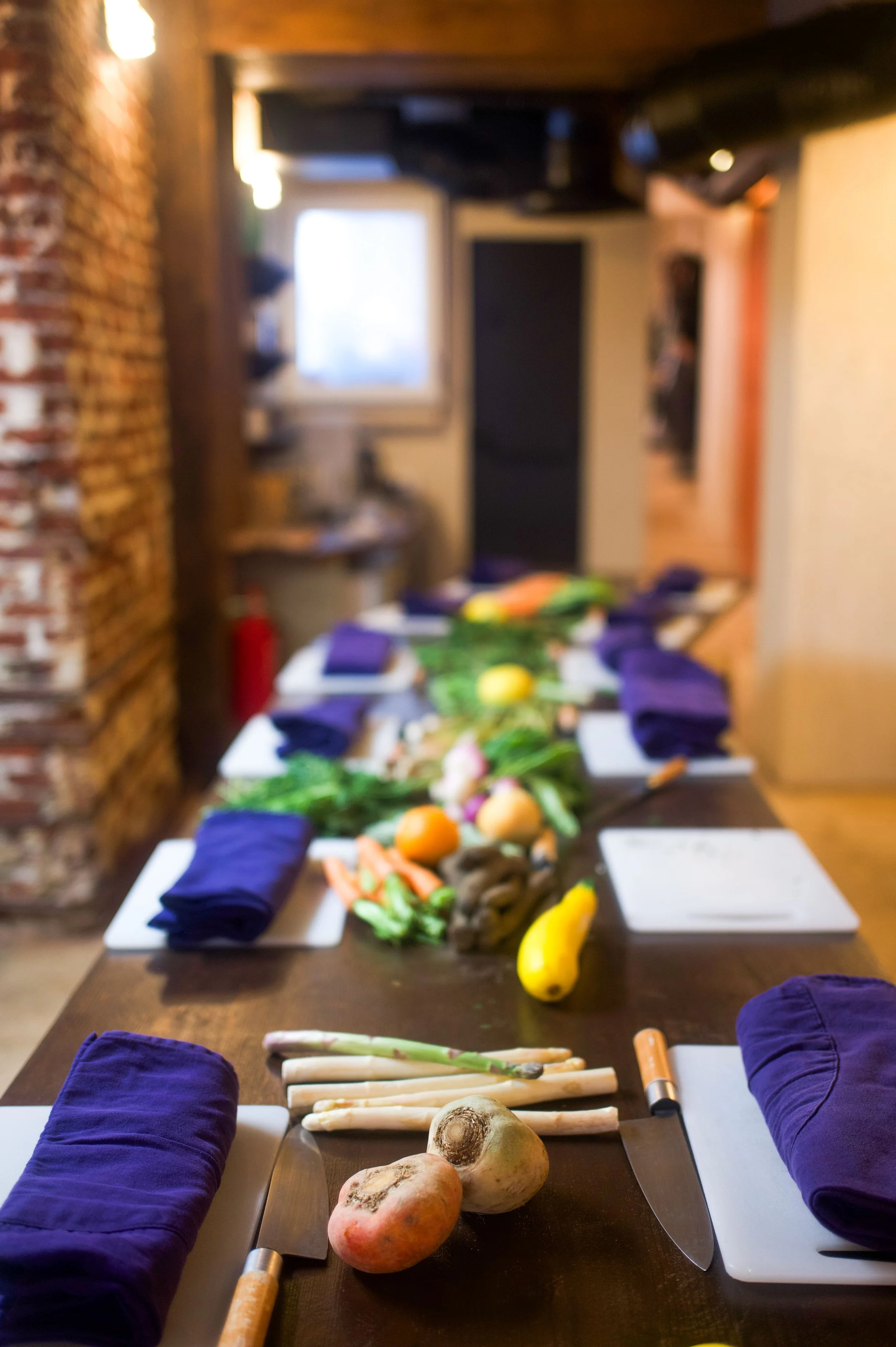 Table à manger avec des légumes frais et des sets de table violets, dans une salle à manger rustique.