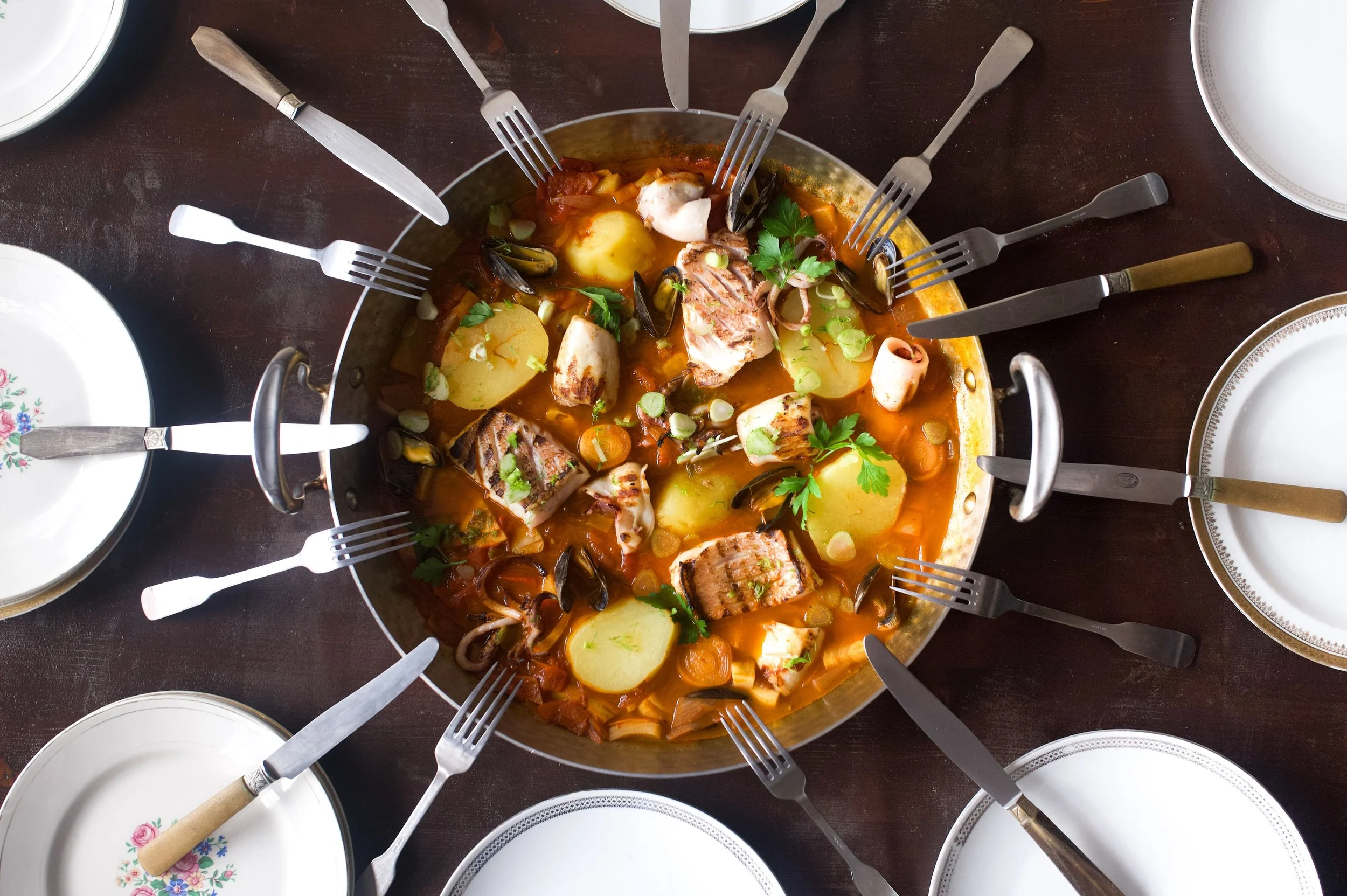 Un plat de soupe de poisson avec des morceaux de poisson, des pommes de terre et des légumes, entouré de plusieurs fourchettes.