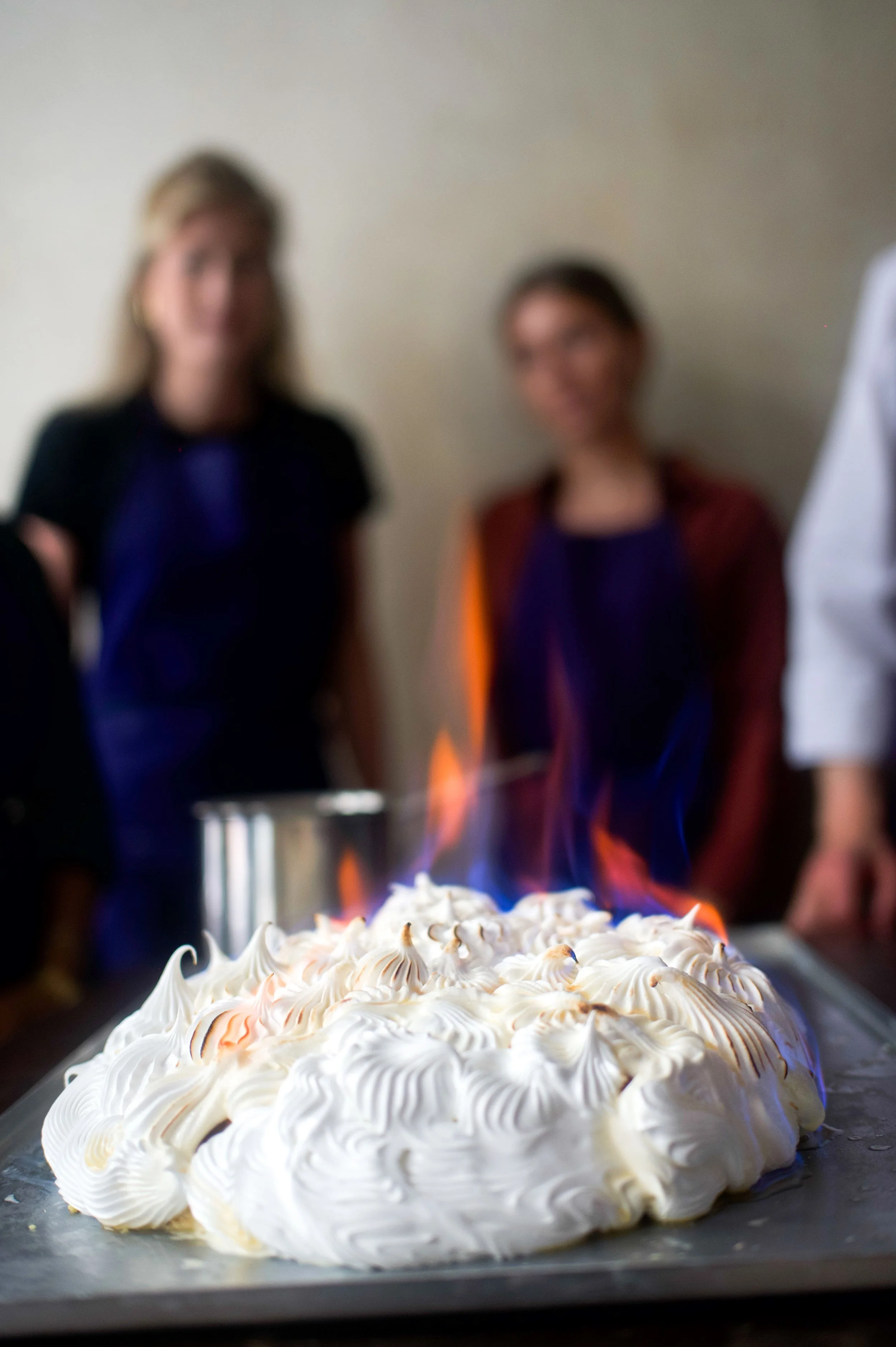 Un gâteau de meringue en flamme avec des personnes floues en arrière-plan.