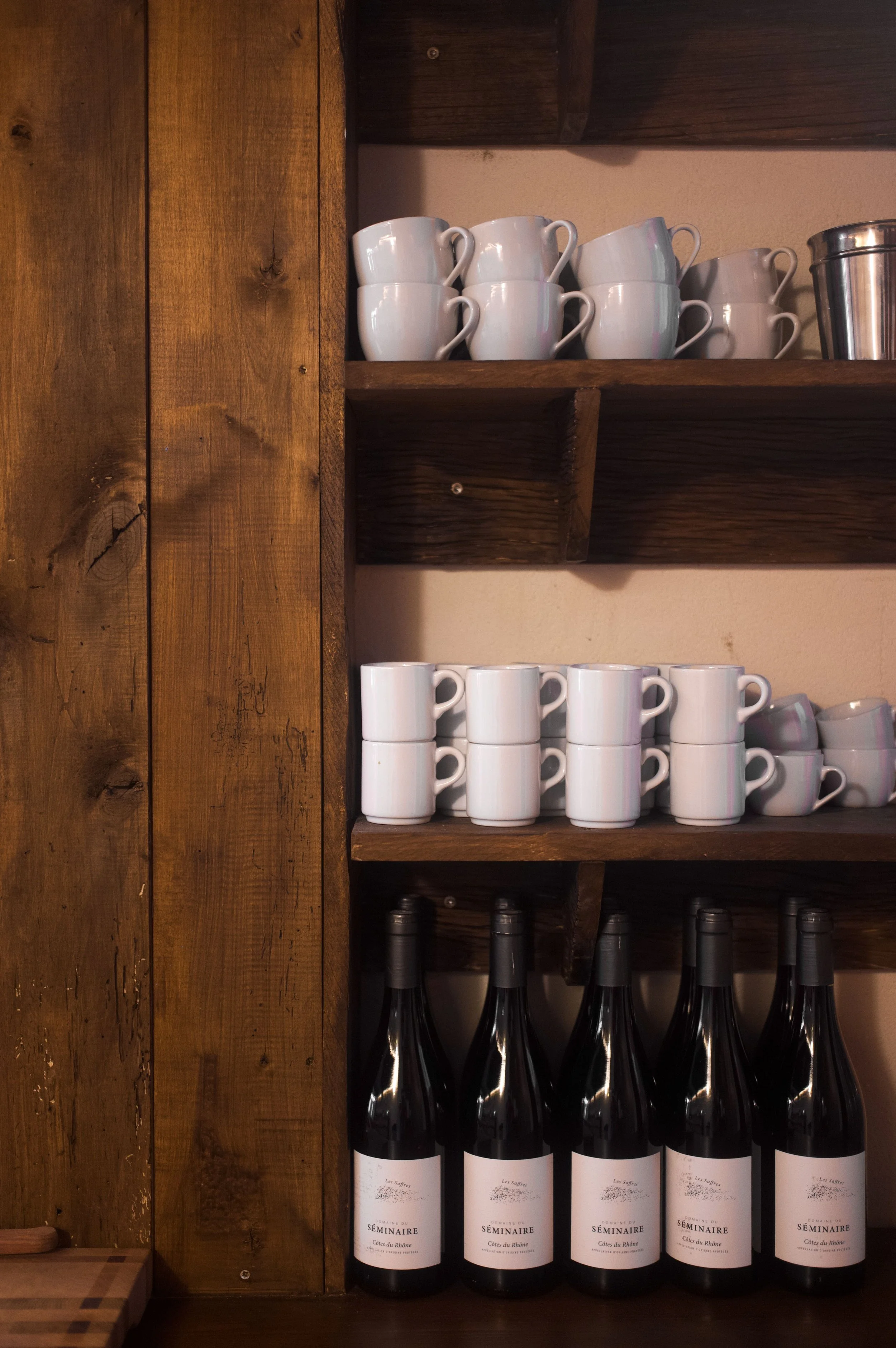 Wooden shelf with white cups, wine bottles and metal container