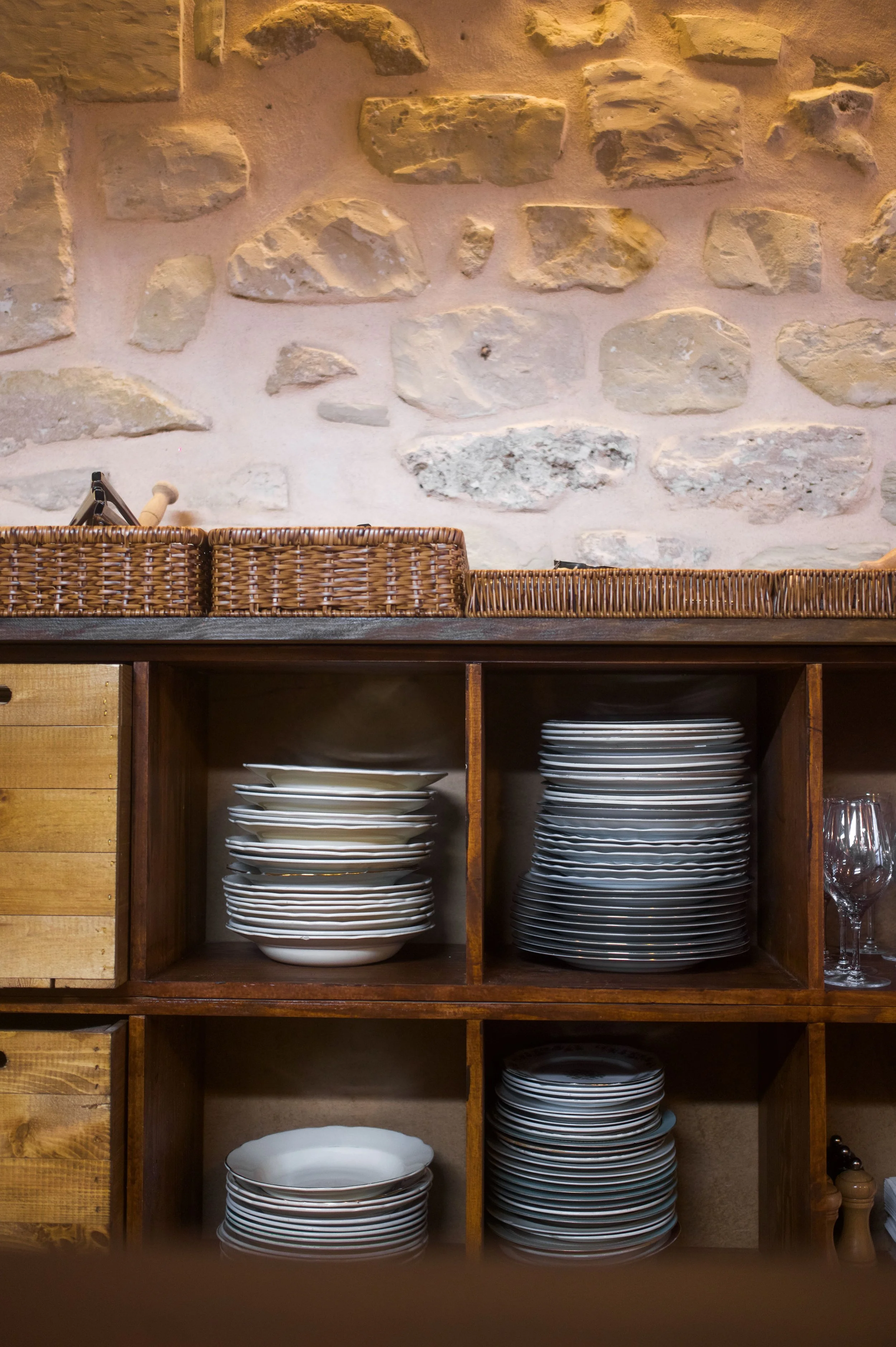 Rack filled with stacked white plates, against a beige stone wall.