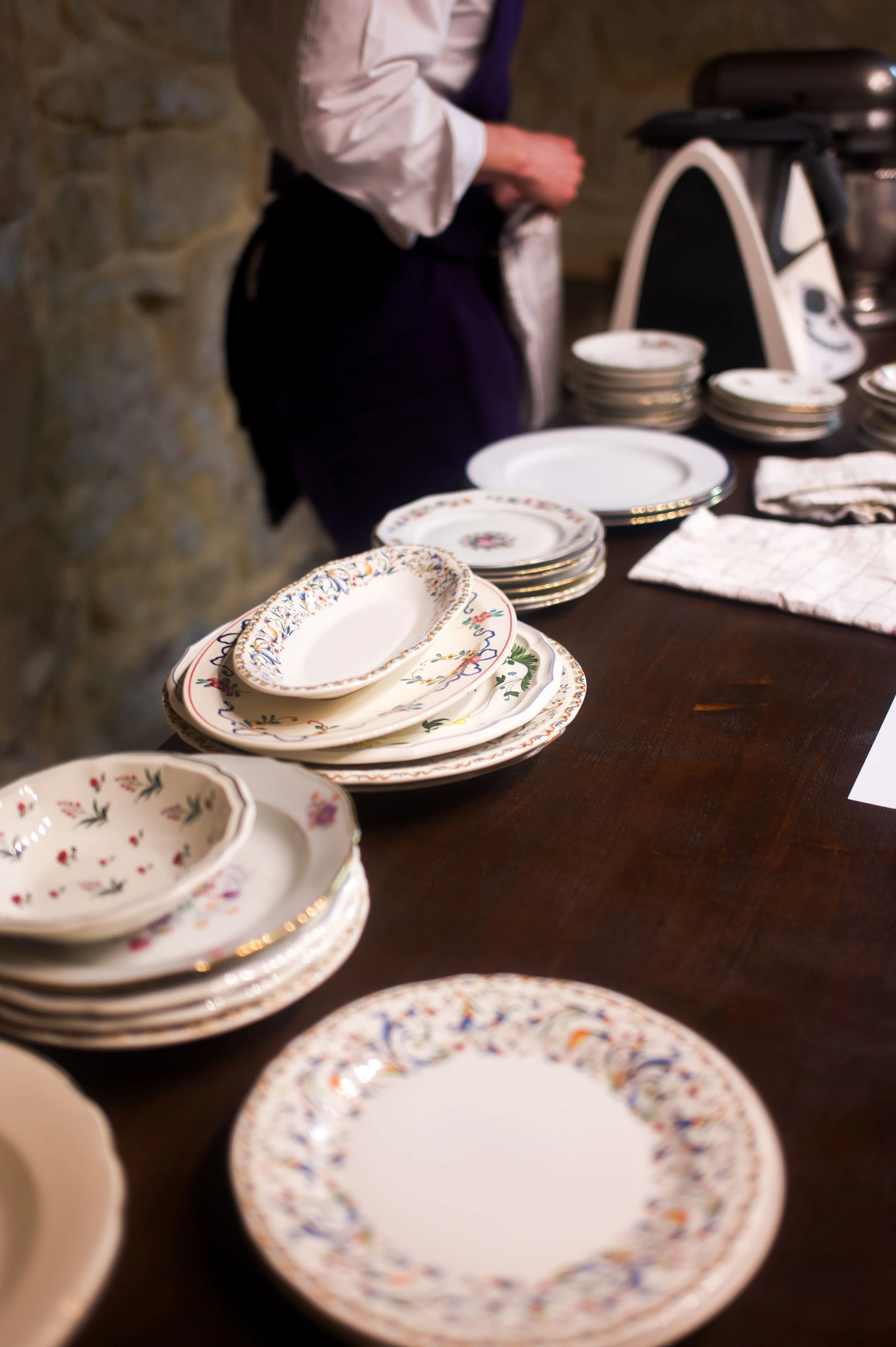 Assiettes en porcelain avec des motifs floraux et des bordures dorées empilées sur une table en bois.