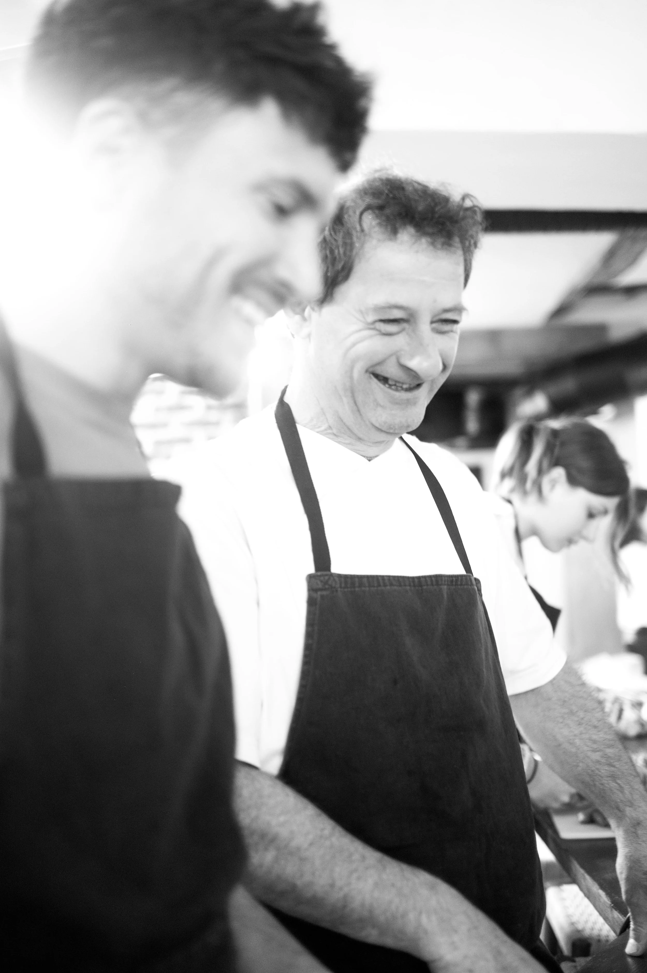 Groupe de personnes souriantes, portant des tabliers, en train de cuisiner ou de travailler en cuisine.