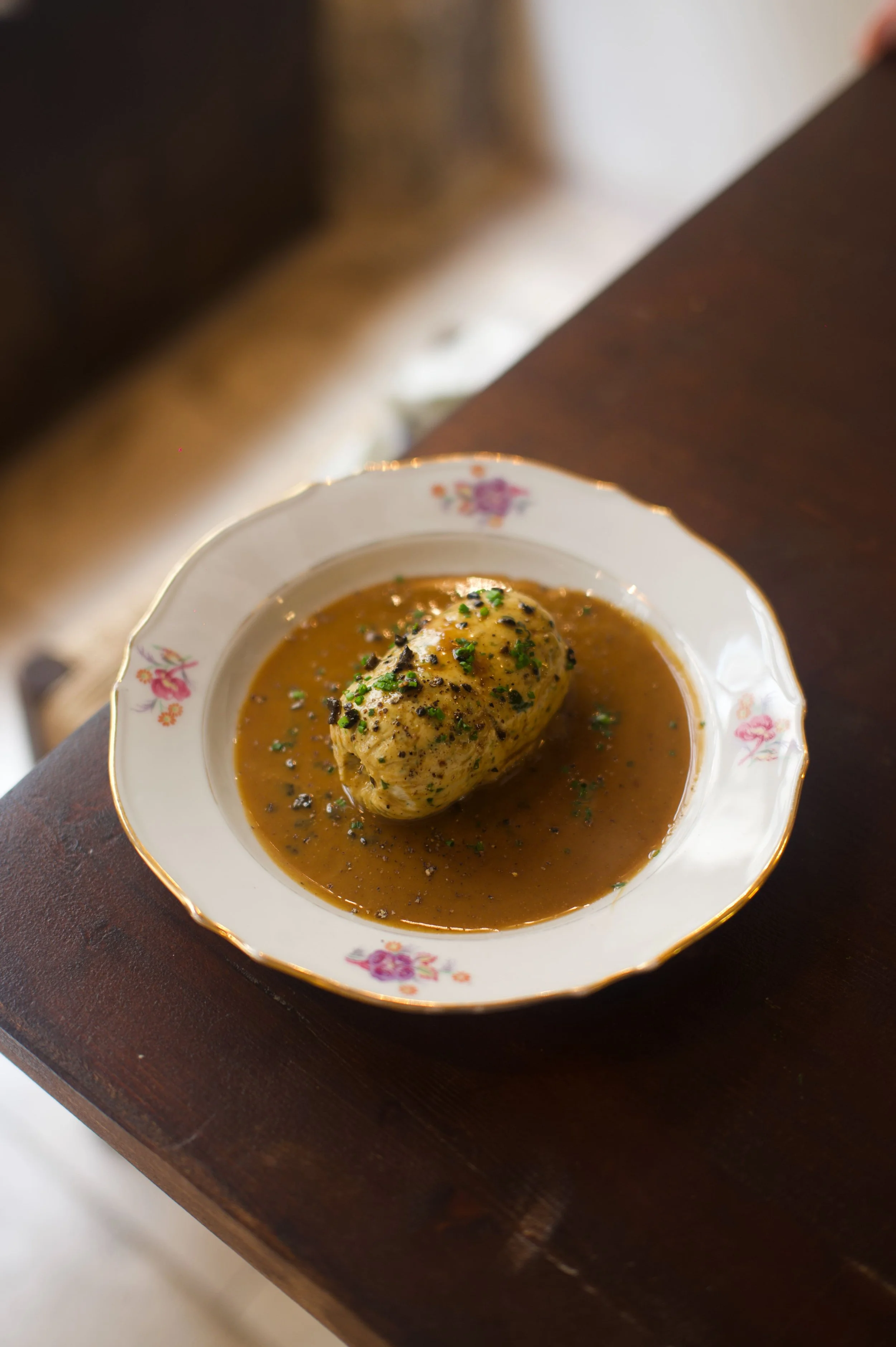 Plat avec une grosse boule de nourriture dans une sauce brune, servi dans une assiette ancienne à motifs floraux.