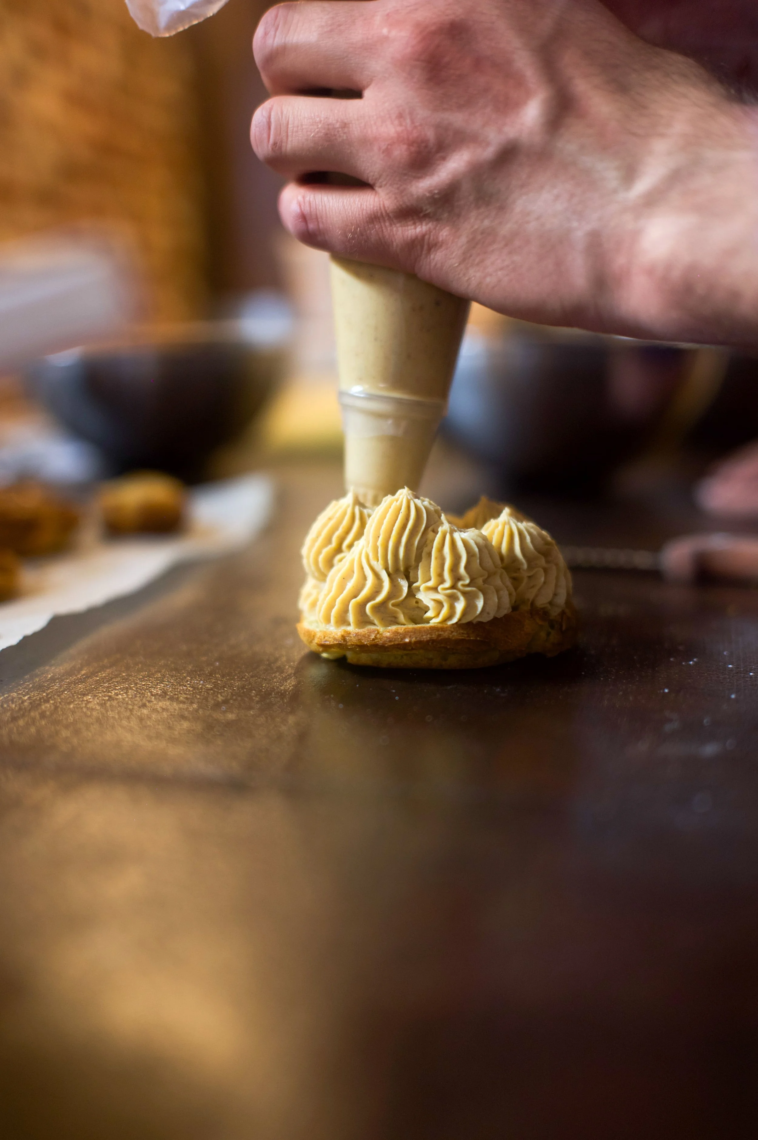 Une personne utilisant une poche à douille pour décorer une petite tarte avec une crème pâtissière ou un glaçage jaune clair.