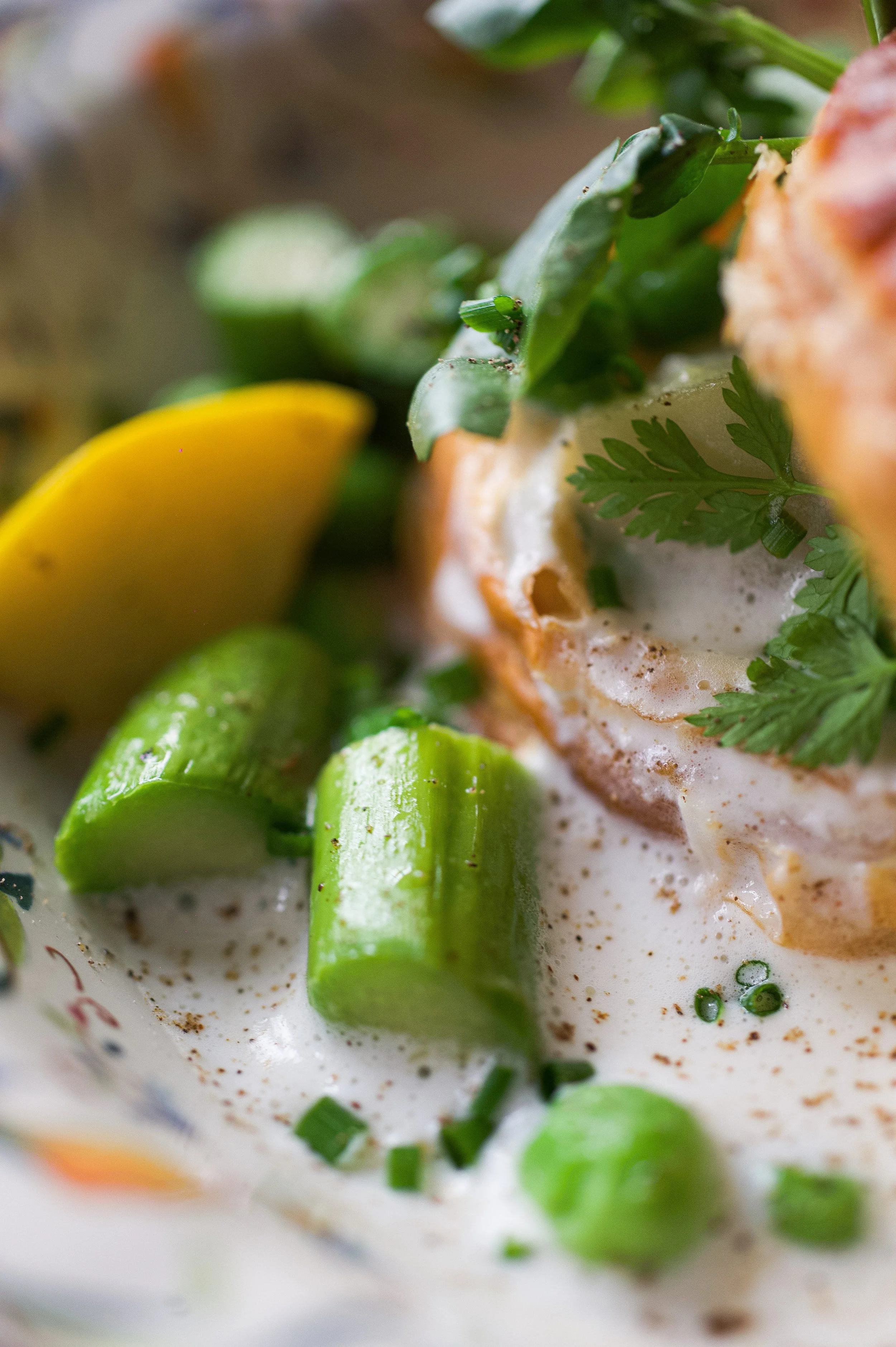 Gros plan d'un plat avec des œufs pochés, de la crème, des herbes fraîches, des morceaux de citron vert et de concombre, présenté dans un bol à décor floral.