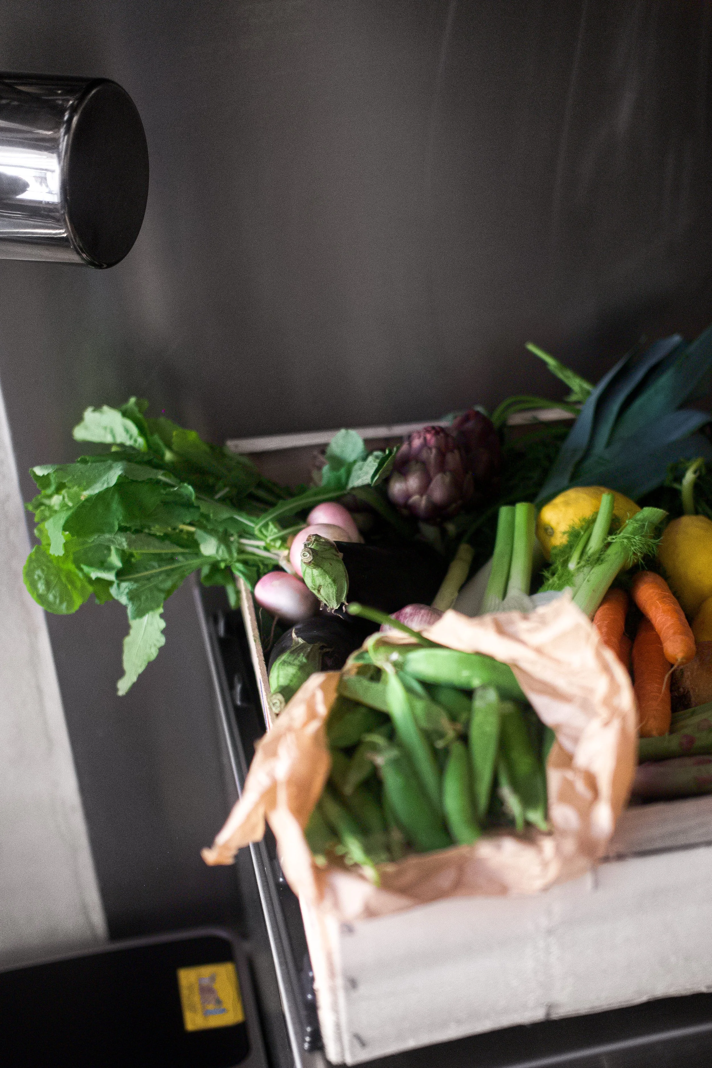 Un panier en bois rempli de légumes frais, dont des carottes, des radis, des oignons verts, de la salade, de l'ananas, un concombre, une courgette et quelques citrons.