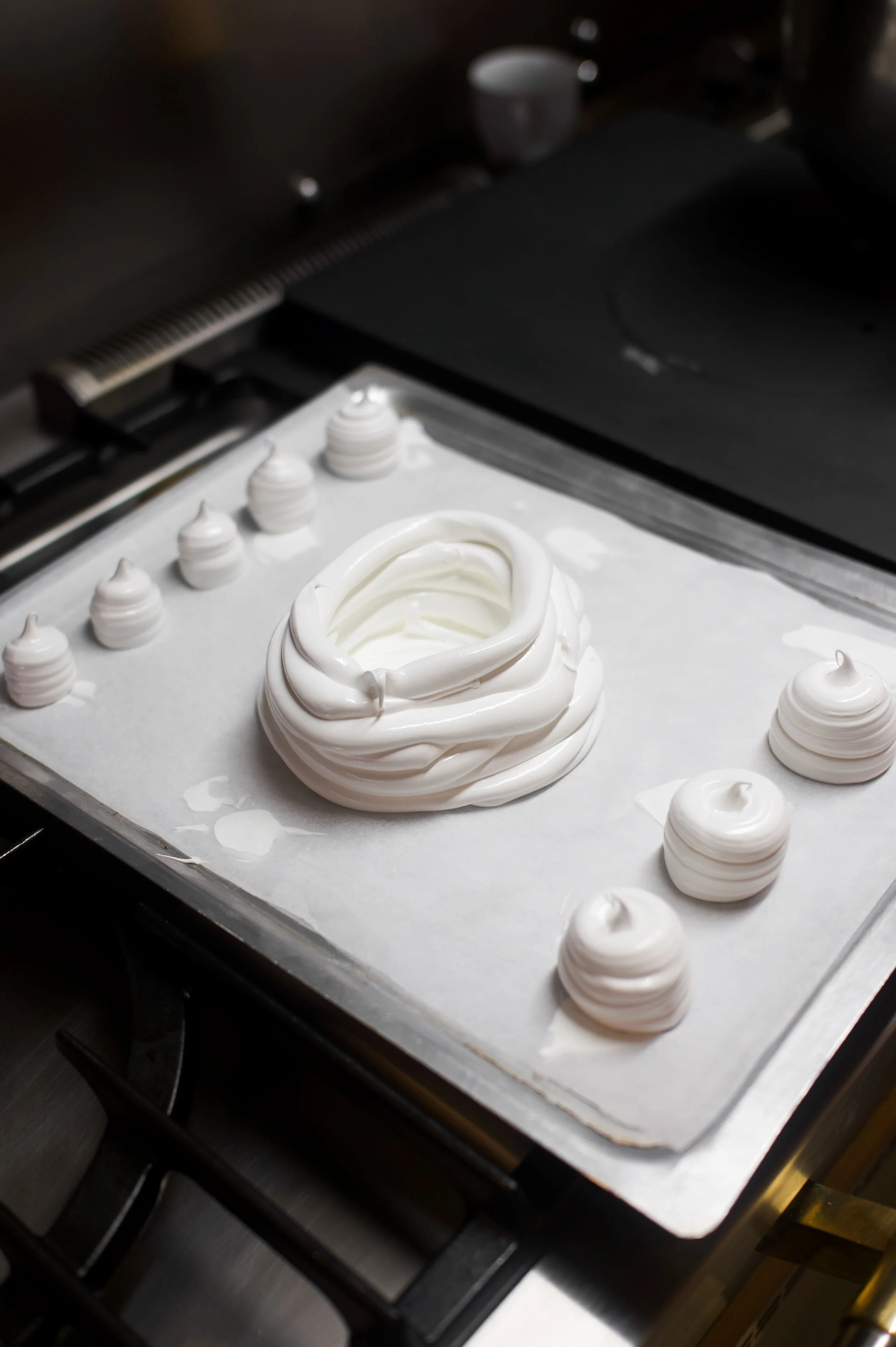 Meringues blanches en cours de fabrication, disposées sur une plaque de cuisson avec du papier sulfurisé, dans une cuisine.
