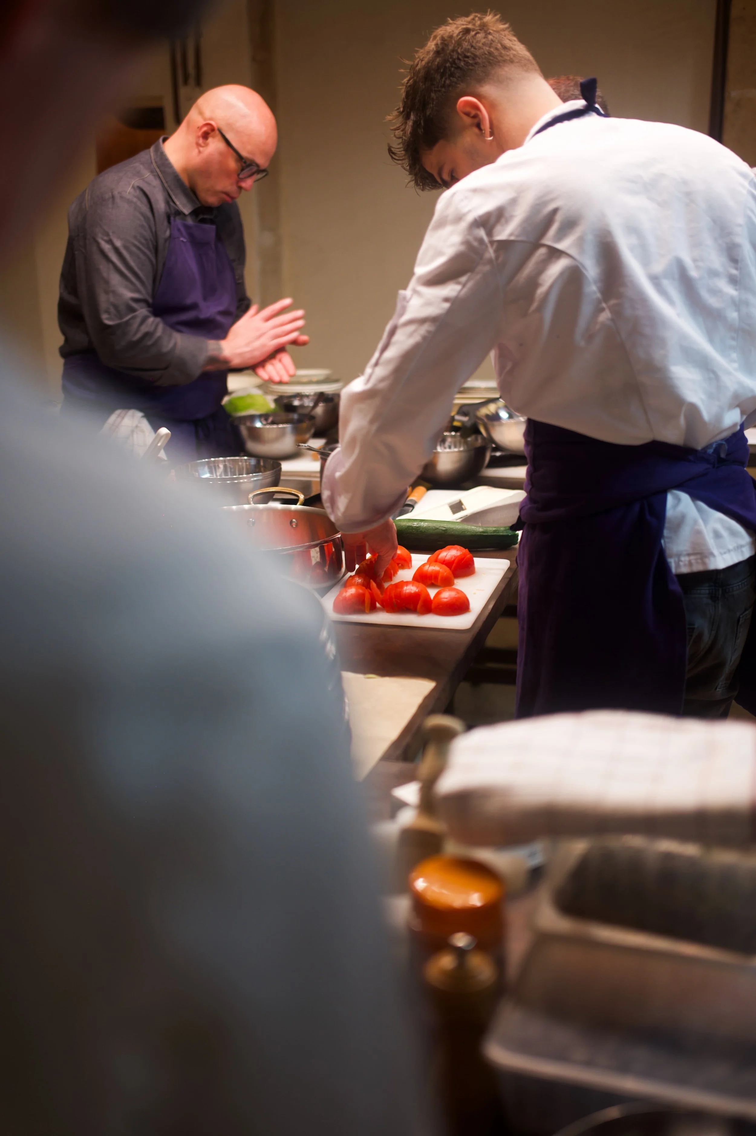 Deux chefs en train de préparer des tomates sur une planche de cuisine dans une cuisine professionnelle.