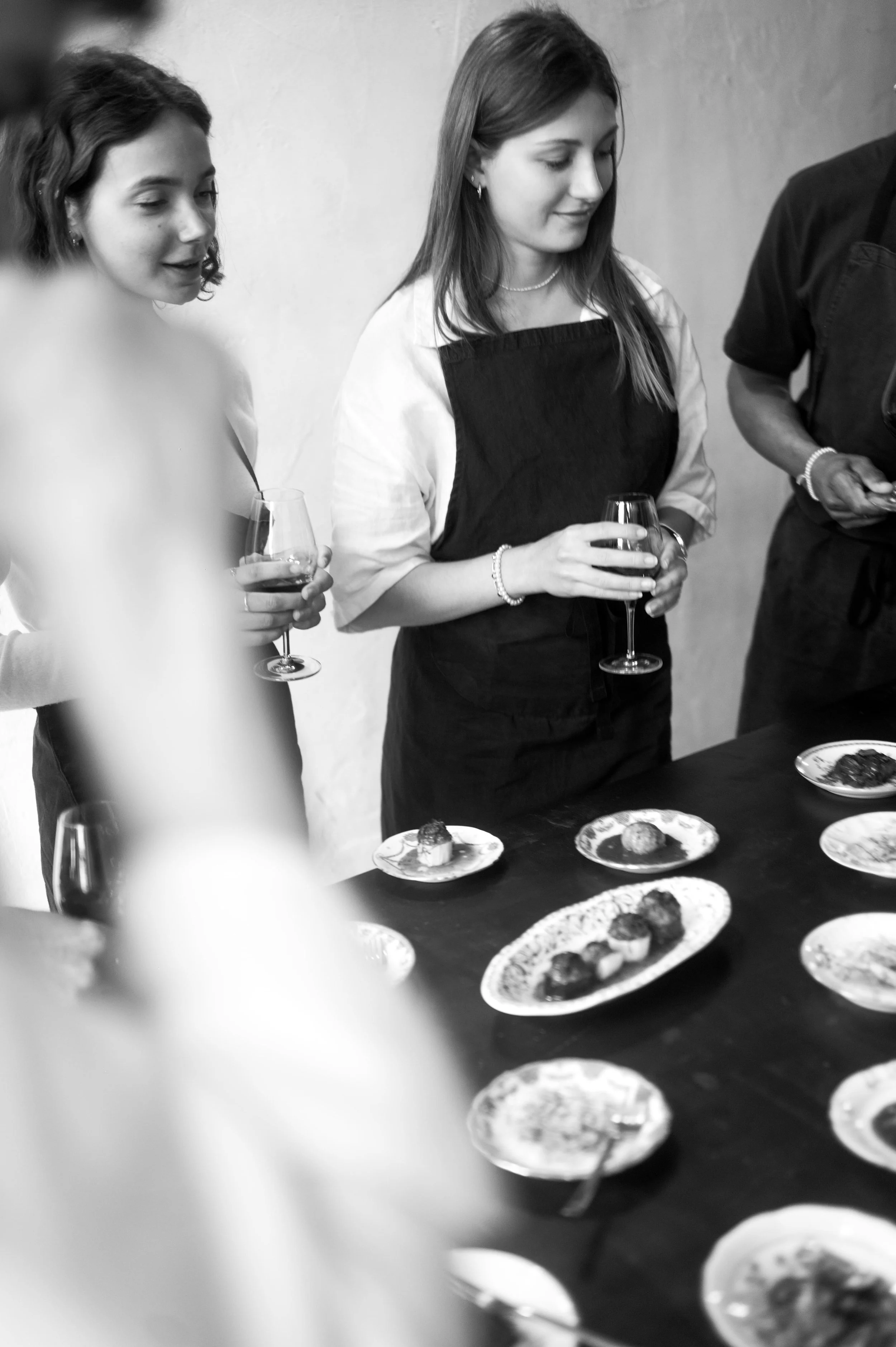 Groupe de jeunes femmes dégustant des plats lors d'une dégustation ou d'un événement culinaire, tenant des verres de vin, avec des petits plats de nourriture sur la table.