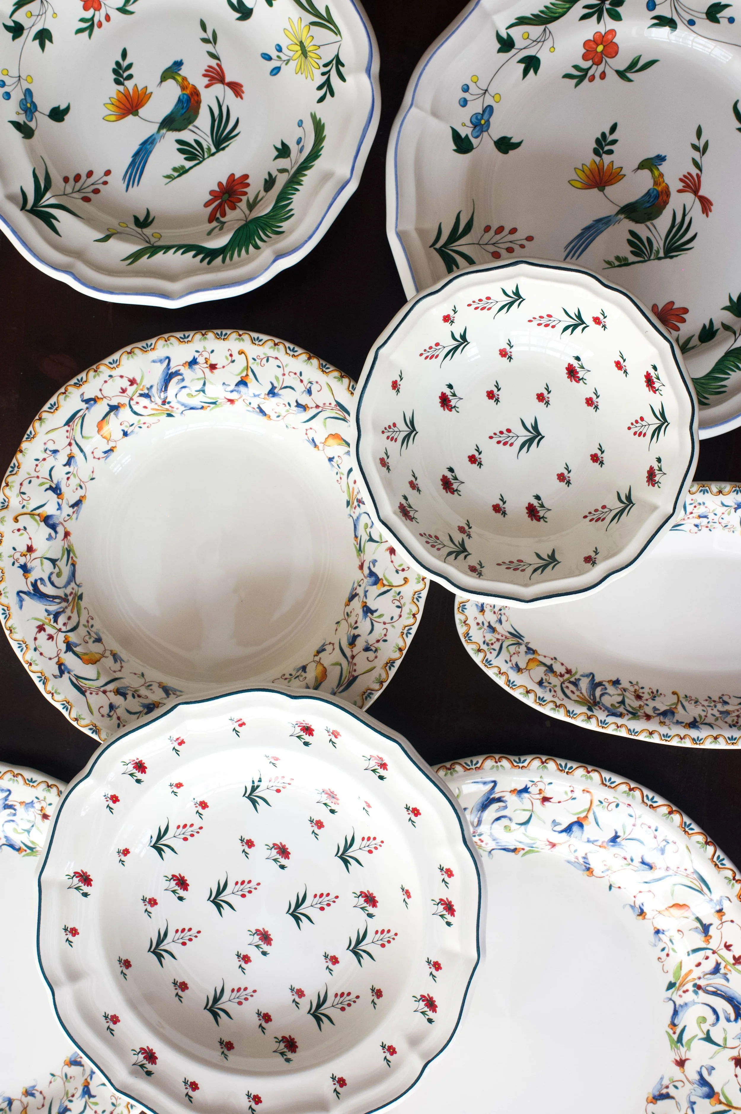 Assiettes en porcelaine avec des motifs floraux et des oiseaux colorés, disposées sur une surface sombre.
