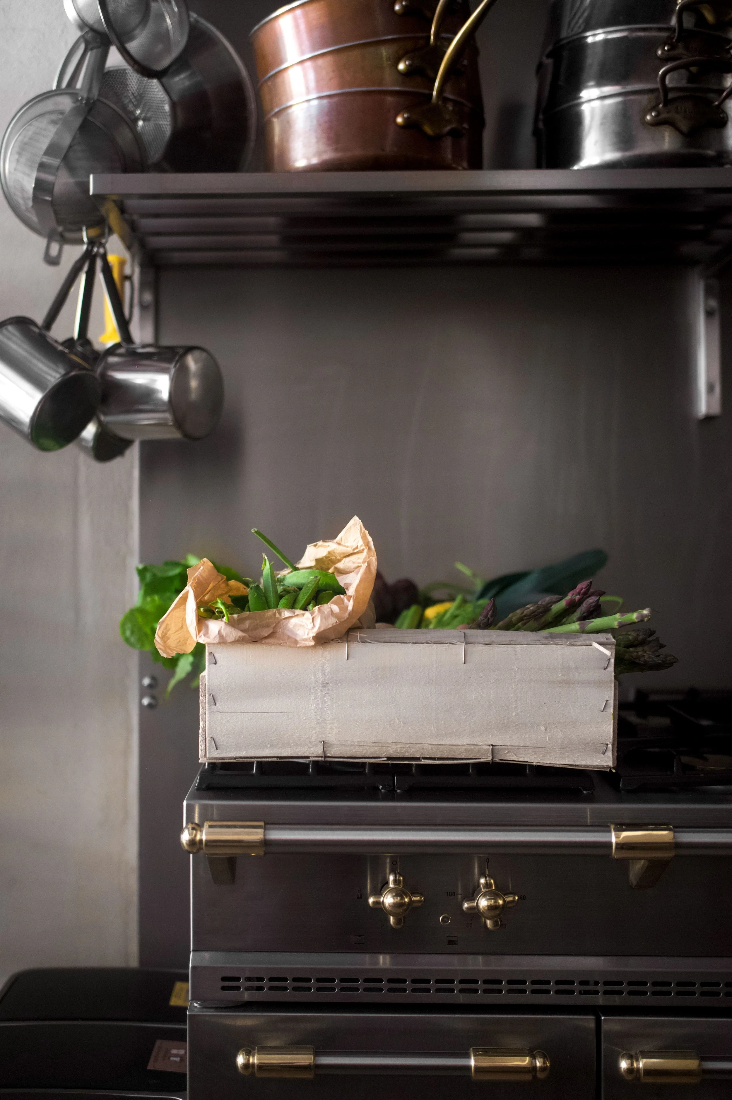 Une boîte en carton contenant des légumes frais, tels que des asperges et de la laitue, posée sur une cuisinière en acier inoxydable.