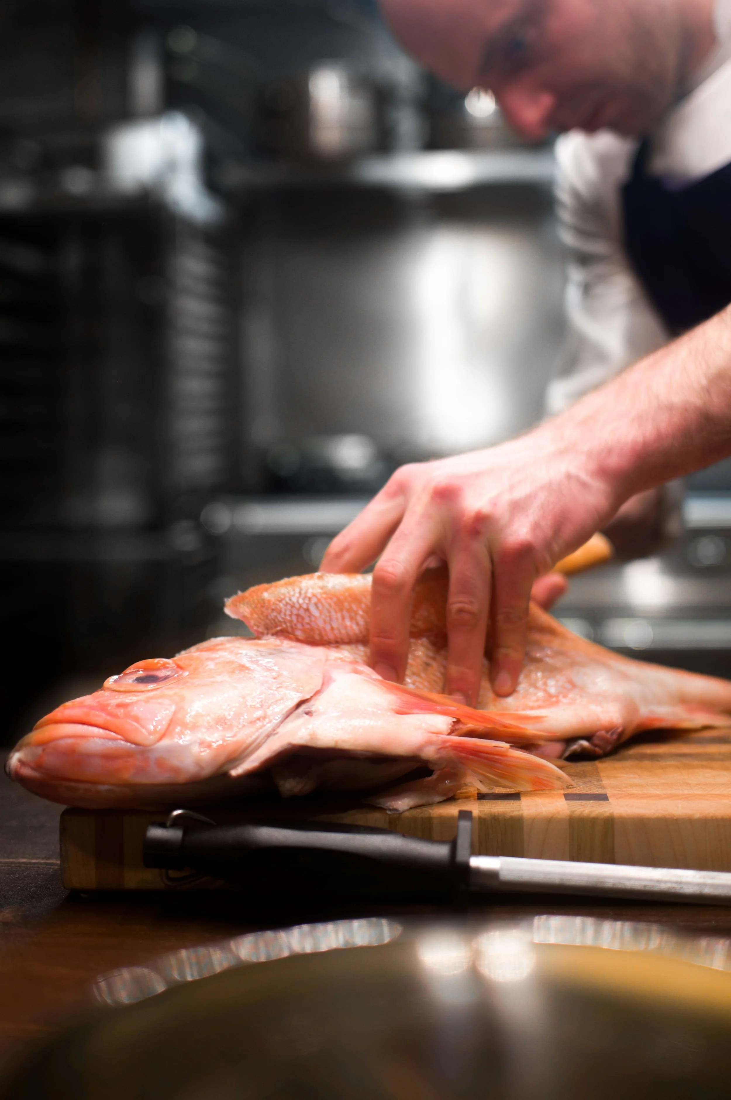 Un chef manipule un poisson frais sur une planche à découper dans une cuisine.