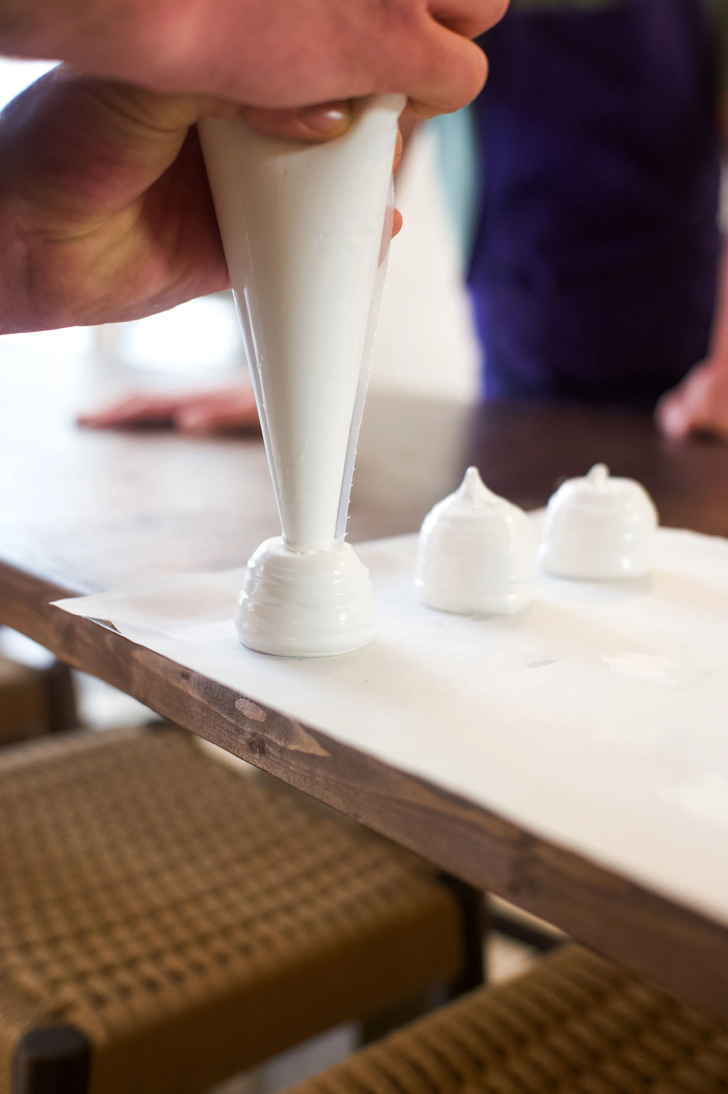 Une personne utilisant une poche à douille pour faire de la pâtisserie, probablement de la meringue ou du gâteau, sur une feuille de papier sulfurisé.