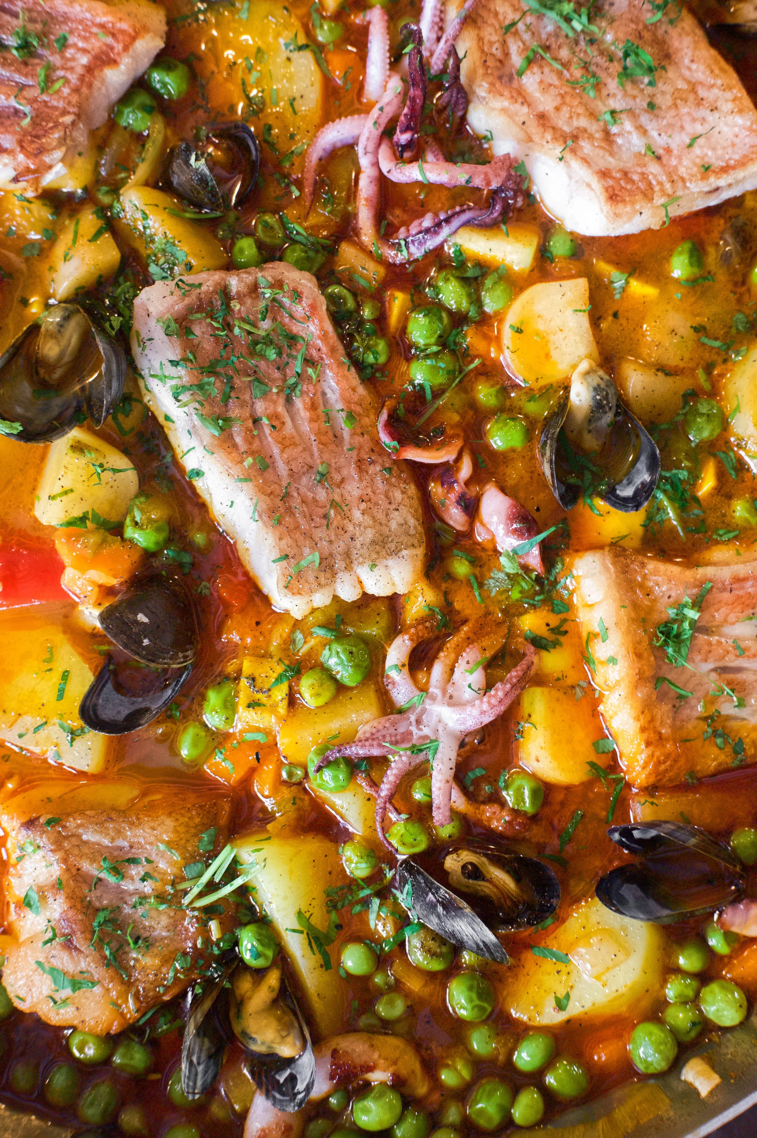 Ragoût de poissons avec pommes de terre, petits pois, calamars, moules et épices, garnie de persil.