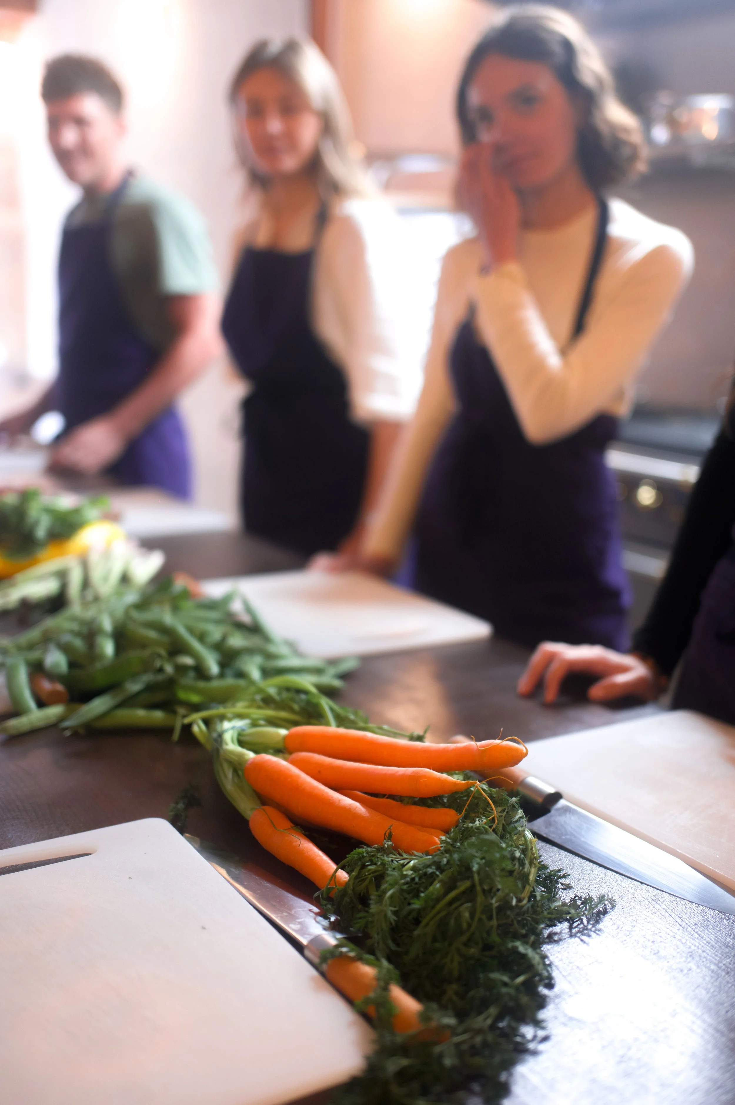 Groupe de personnes en cuisine, avec un plan de carottes fraîches sur une table.