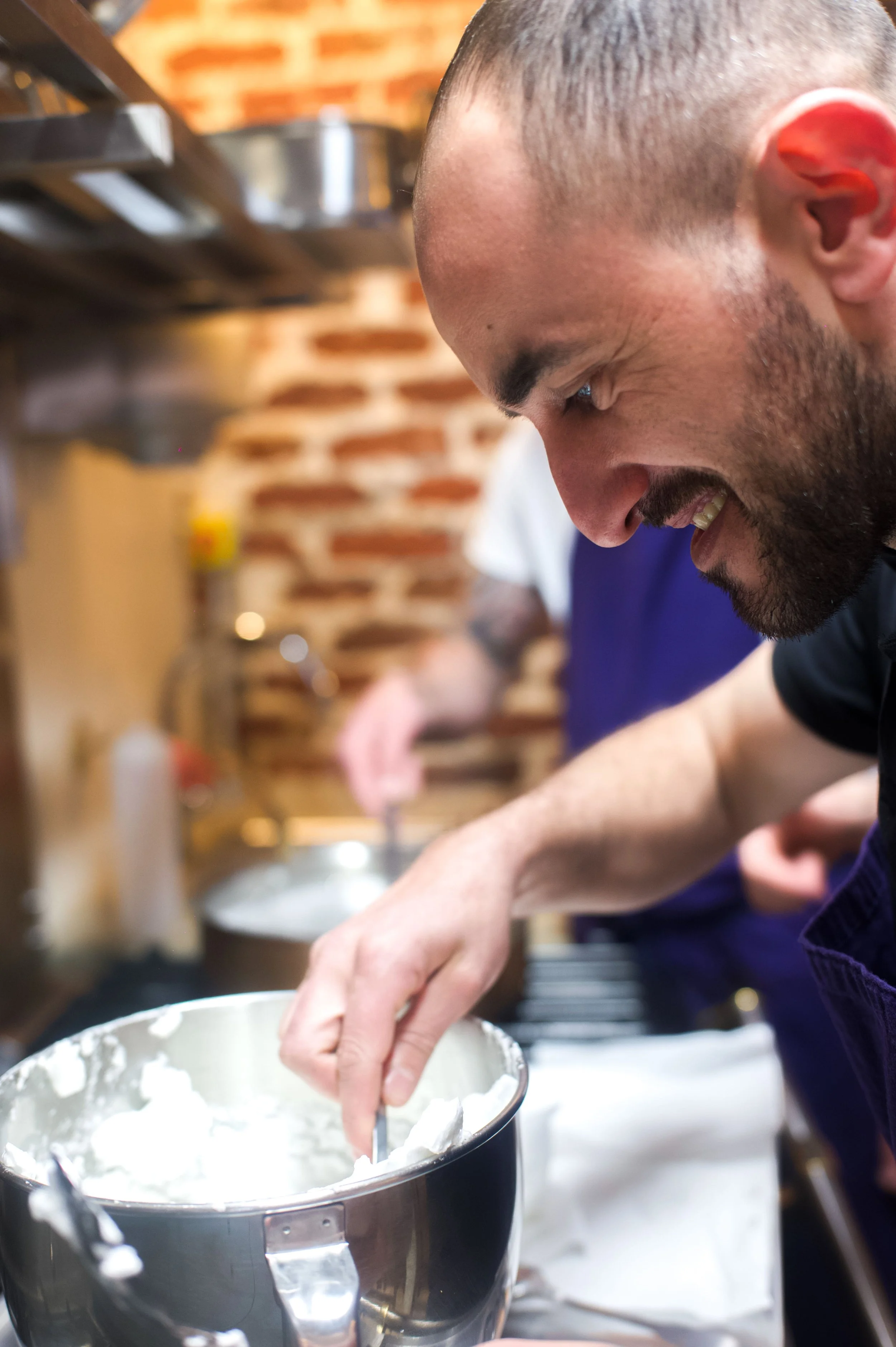 Un homme souriant en train de mélanger de la crème dans un bol en inox dans une cuisine.