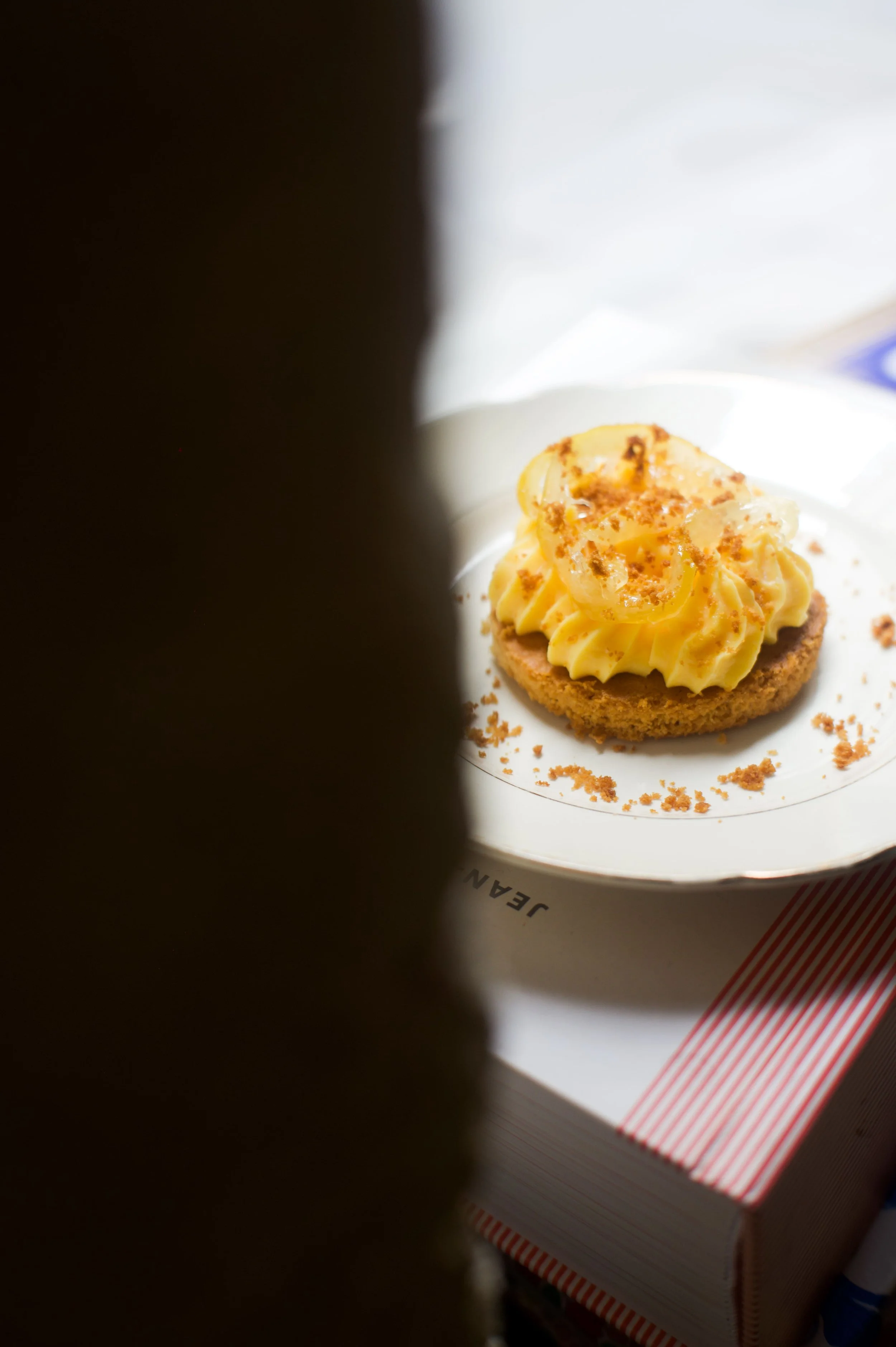 Un dessert sur une assiette, avec une base circulaire et une garniture de crème jaune, visible à travers un espace entre deux objets flous.