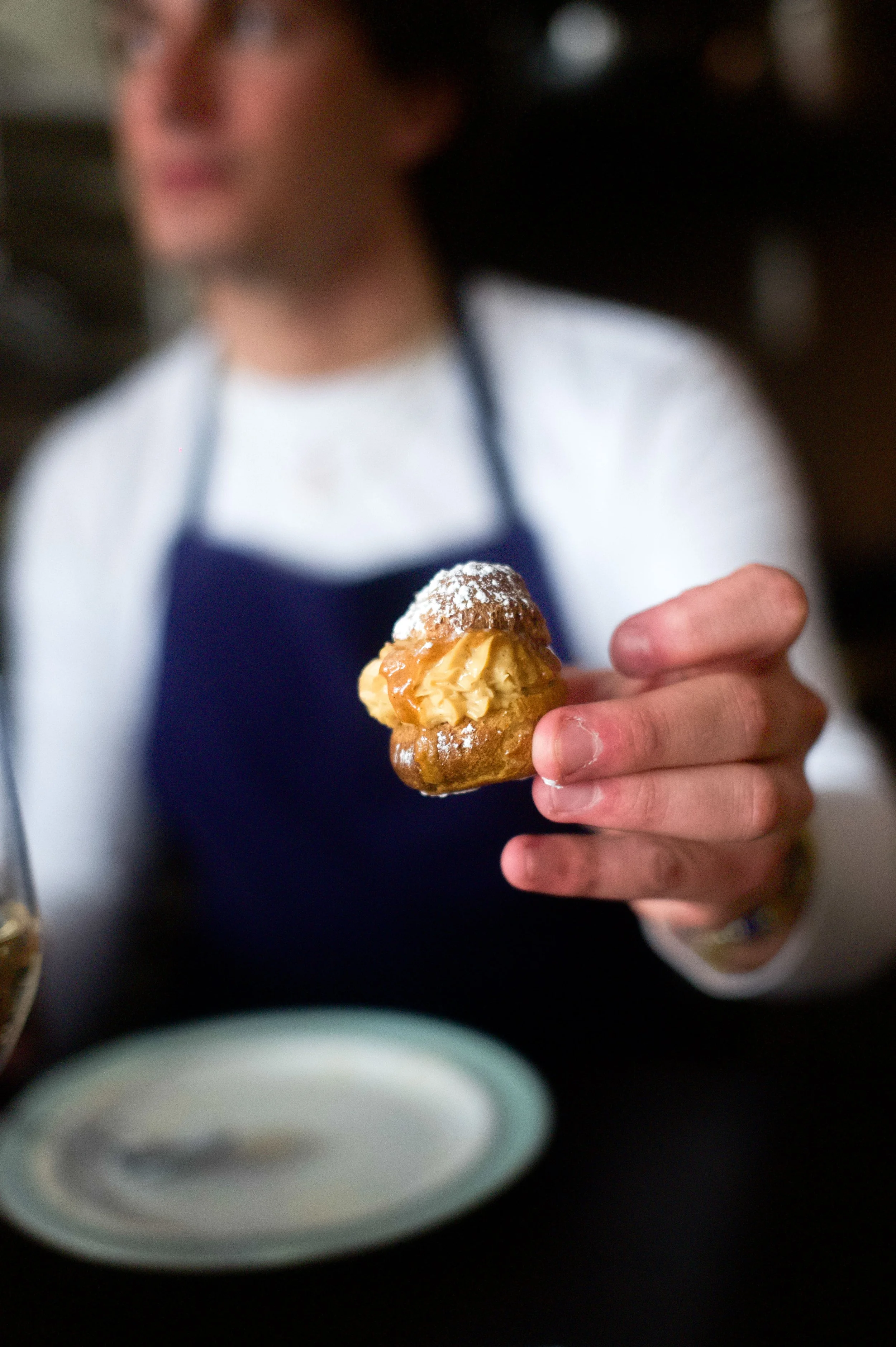 Une personne tient une pâtisserie garnie de crème, saupoudrée de sucre glace, avec un fond flou.