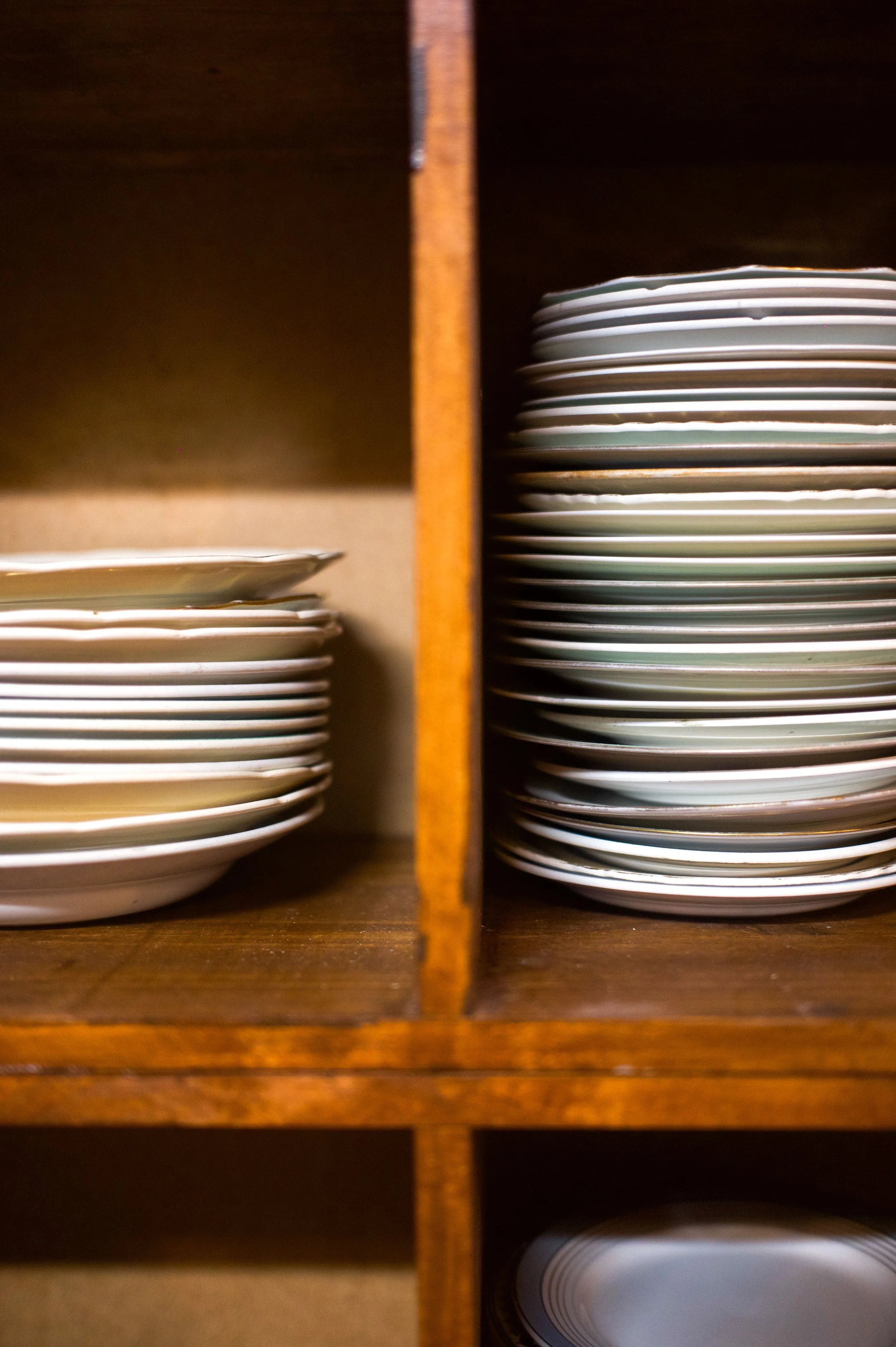 A wooden shelf containing stacks of white porcelain plates.