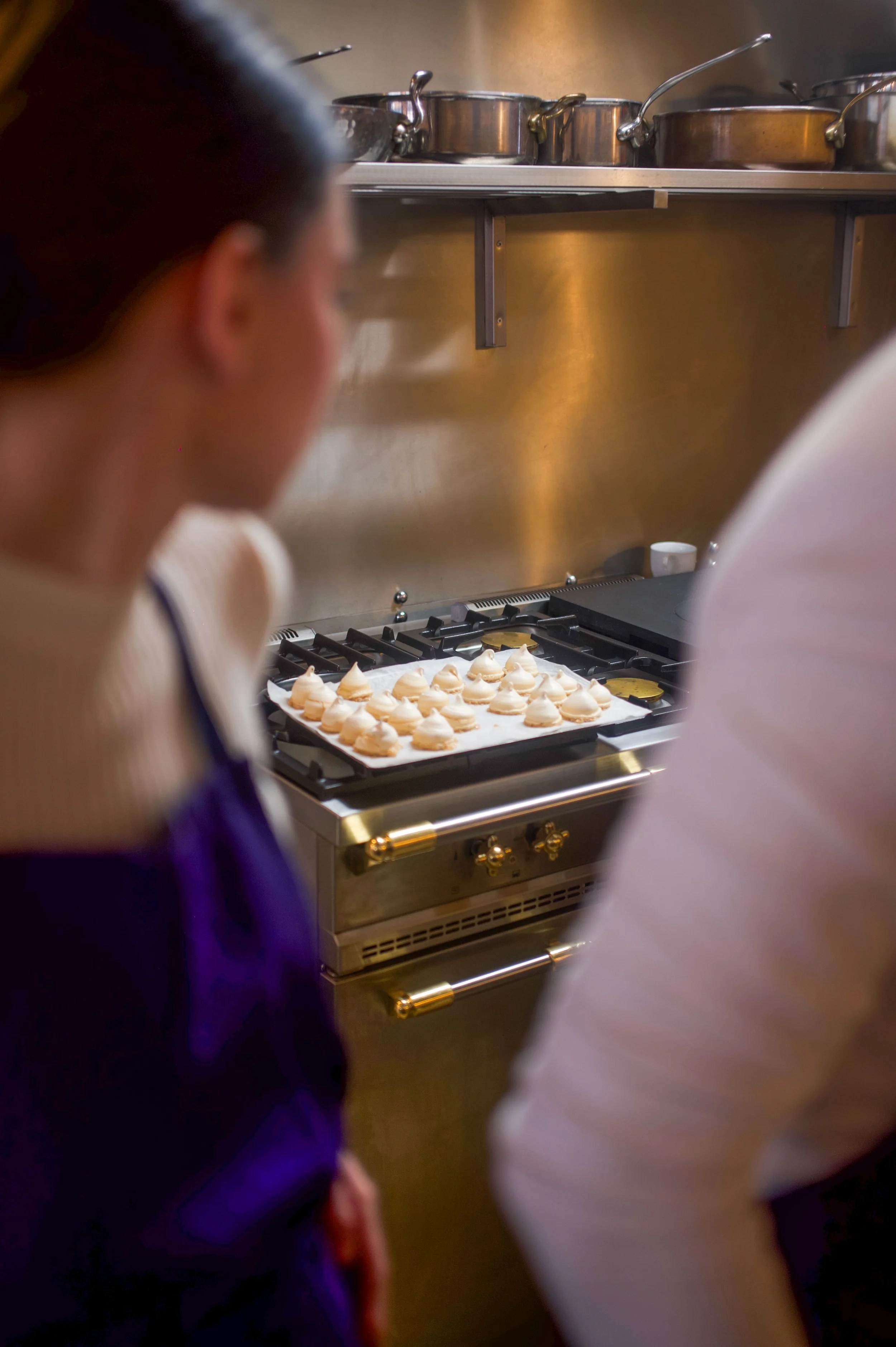 Des éclairs à la crème sur une plaque dans une cuisine, avec deux personnes en premier plan.
