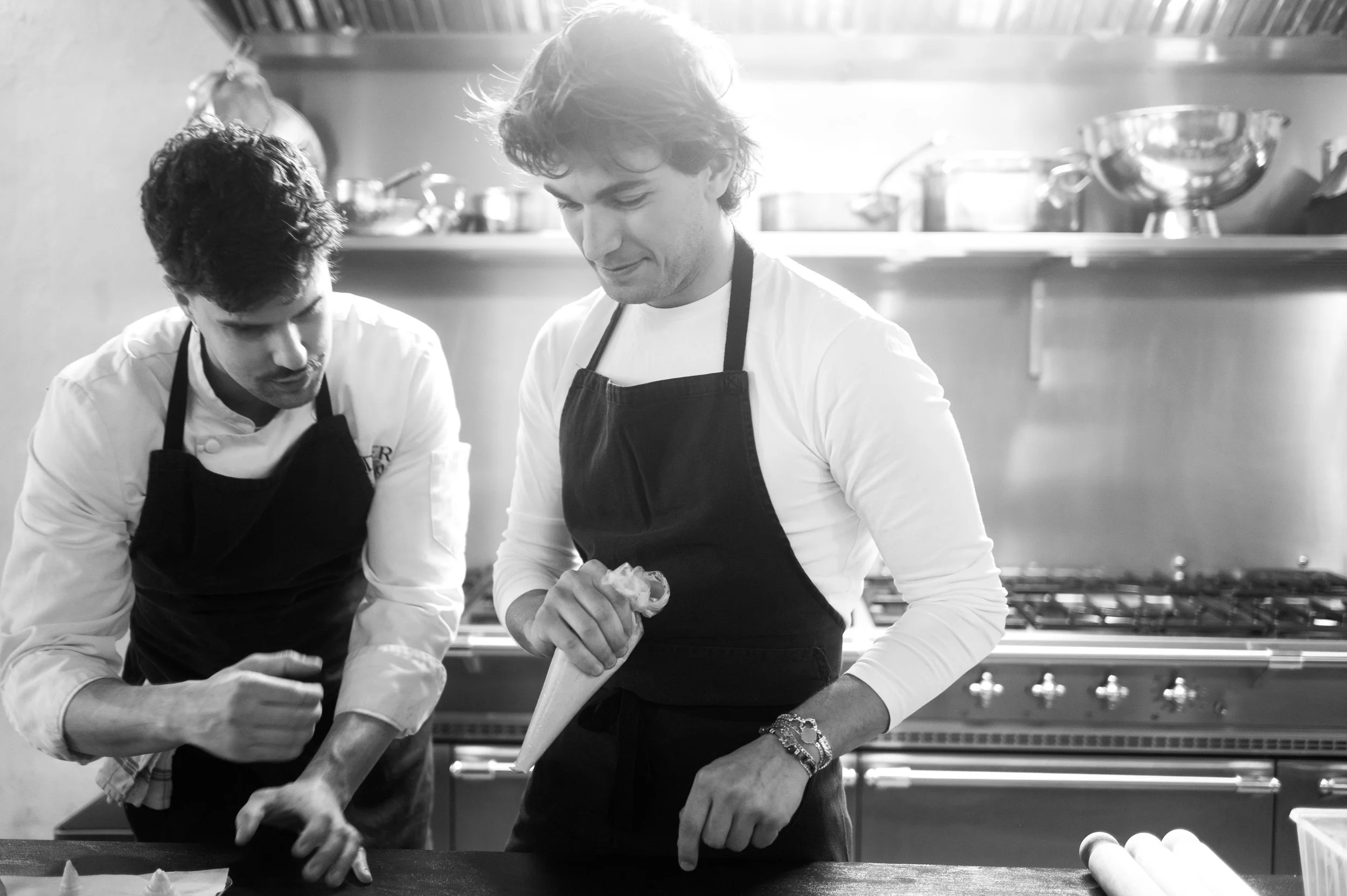 Deux chefs cuisiniers en cuisine, utilisant des sacs de pâtisserie pour préparer des desserts.