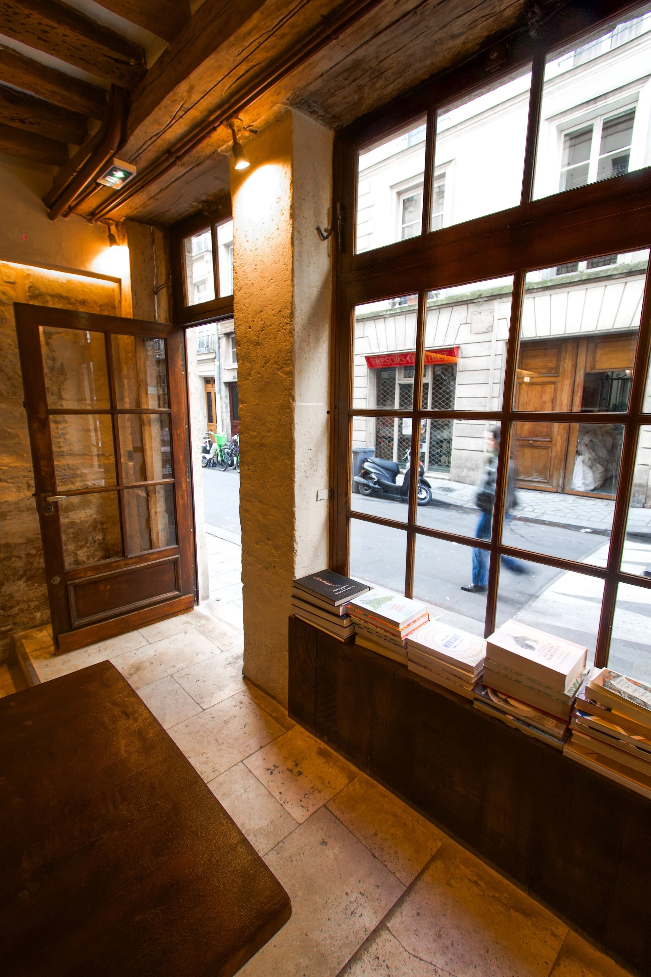 Interior of a café or bookshop with large wooden windows and a counter with books stacked next to the window.