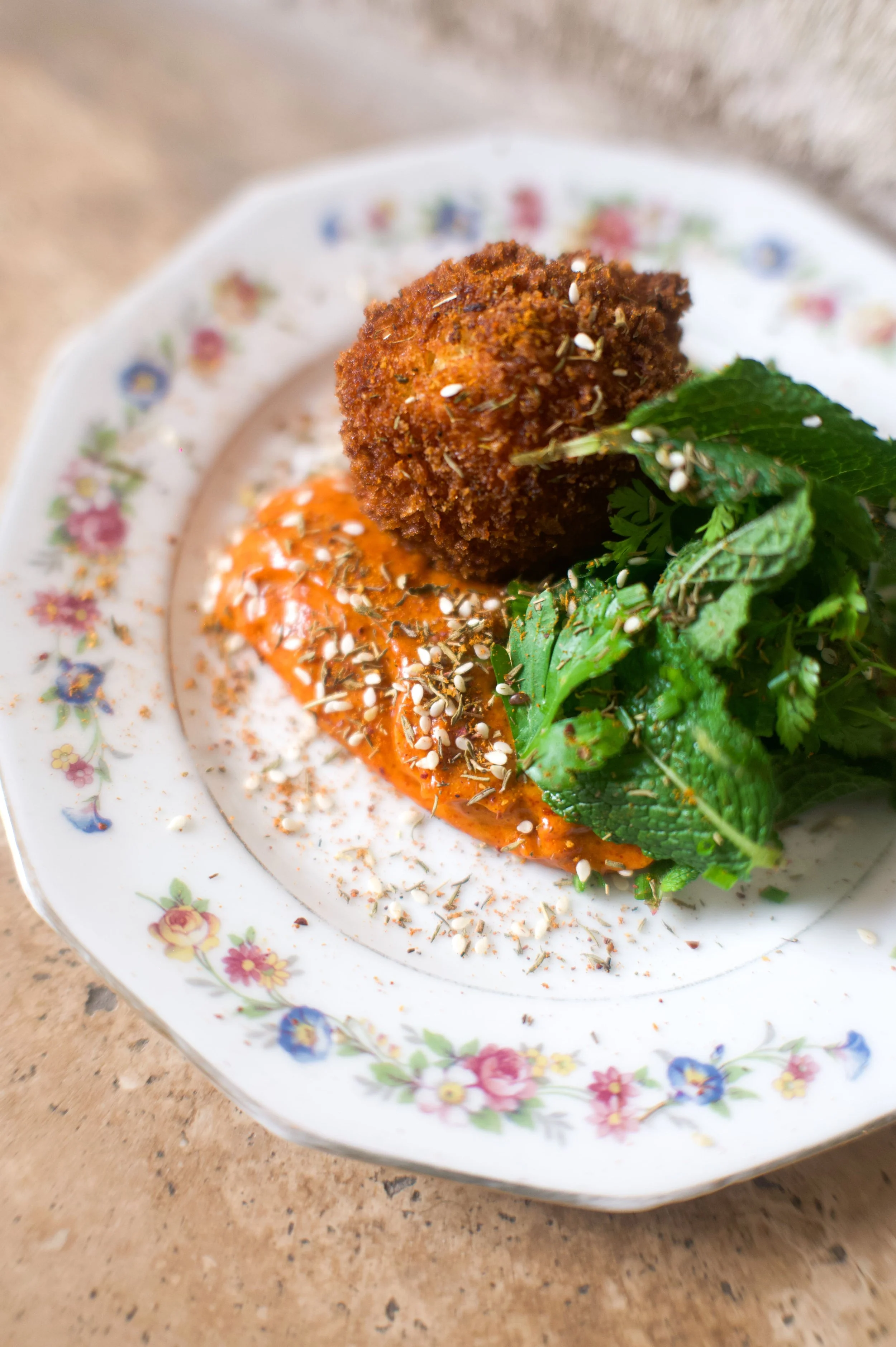 Une assiette en porcelaine avec un plat de falafel, de la sauce rouge, des feuilles de menthe et des graines de sésame.
