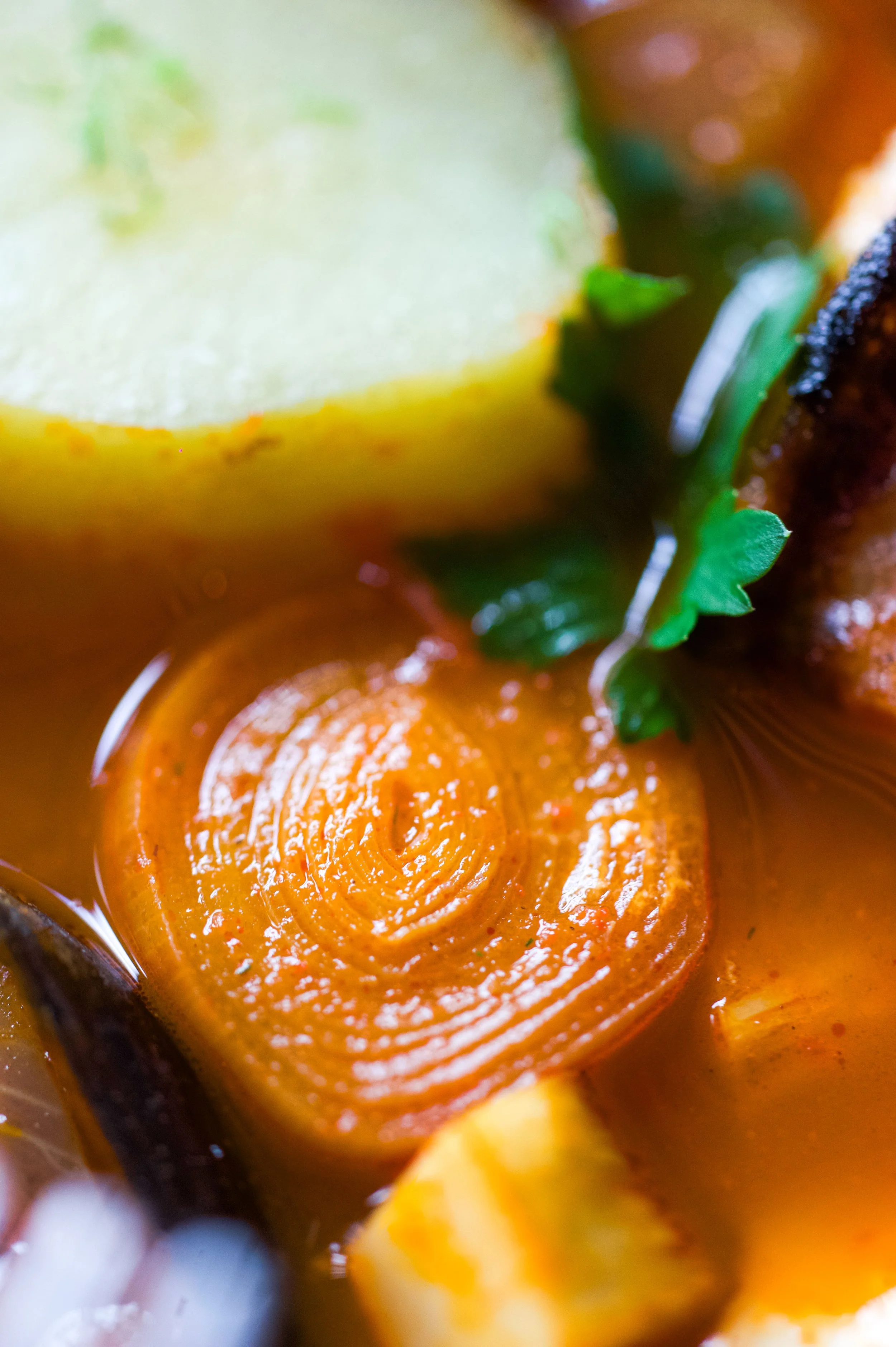 Gros plan d'une sauce char siolée avec une rondelle de citron, une feuille de coriandre, et d'autres ingrédients flous en arrière-plan.