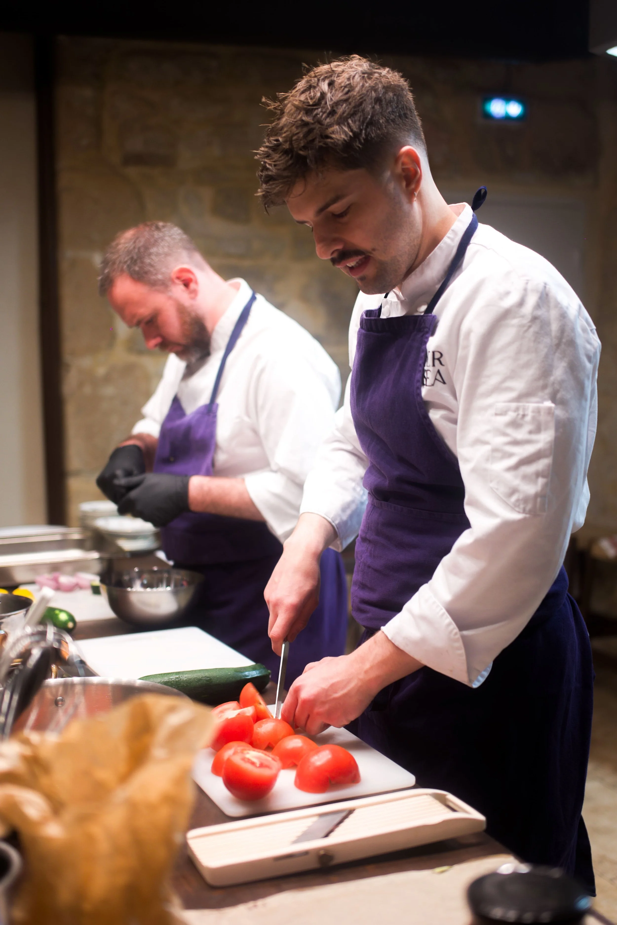 Deux chefs en train de couper des tomates sur une planche à découper dans une cuisine.