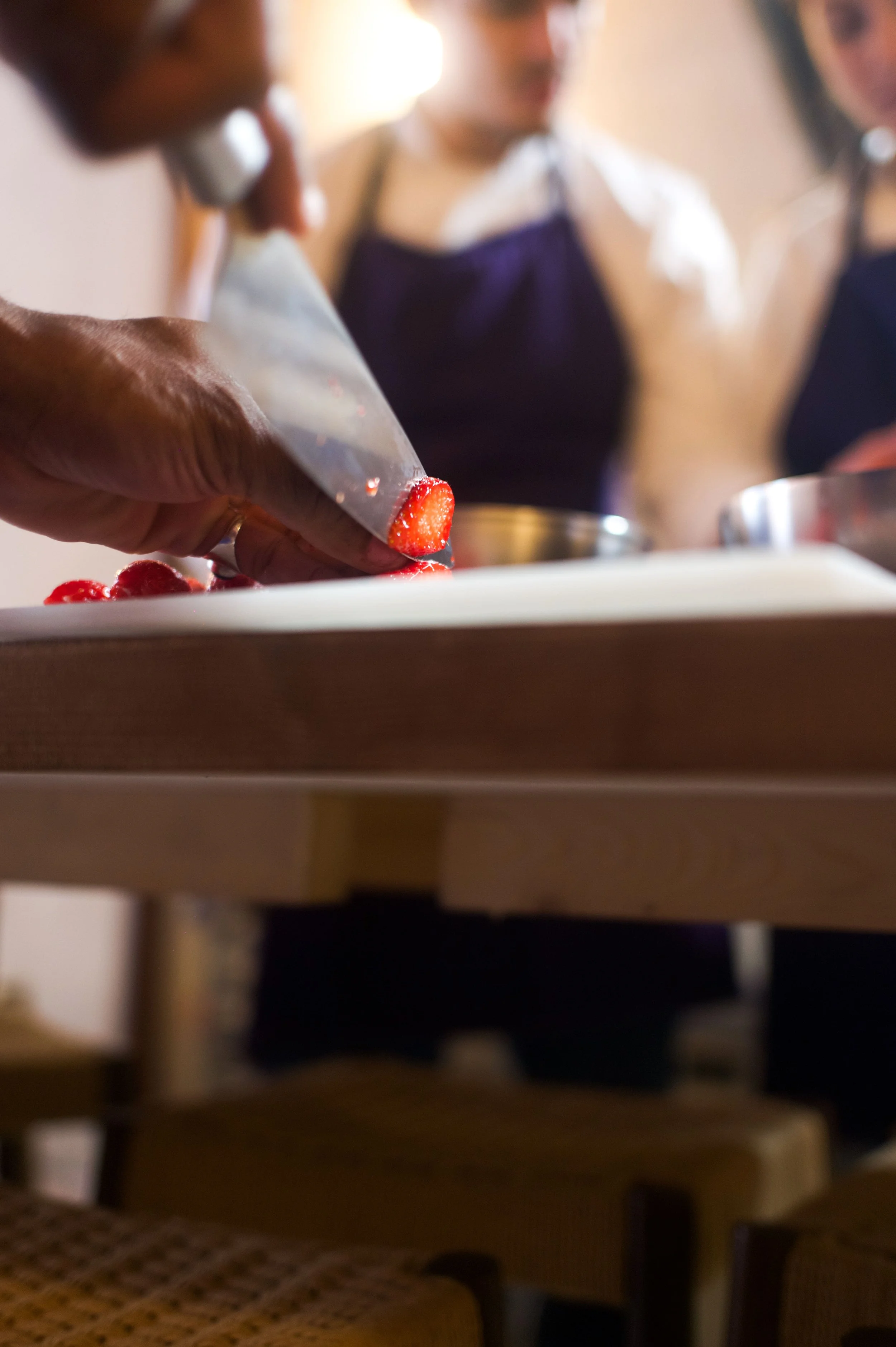 Personnes en tenue de cuisine préparant des fraises coupées, avec deux autres personnes en arrière-plan