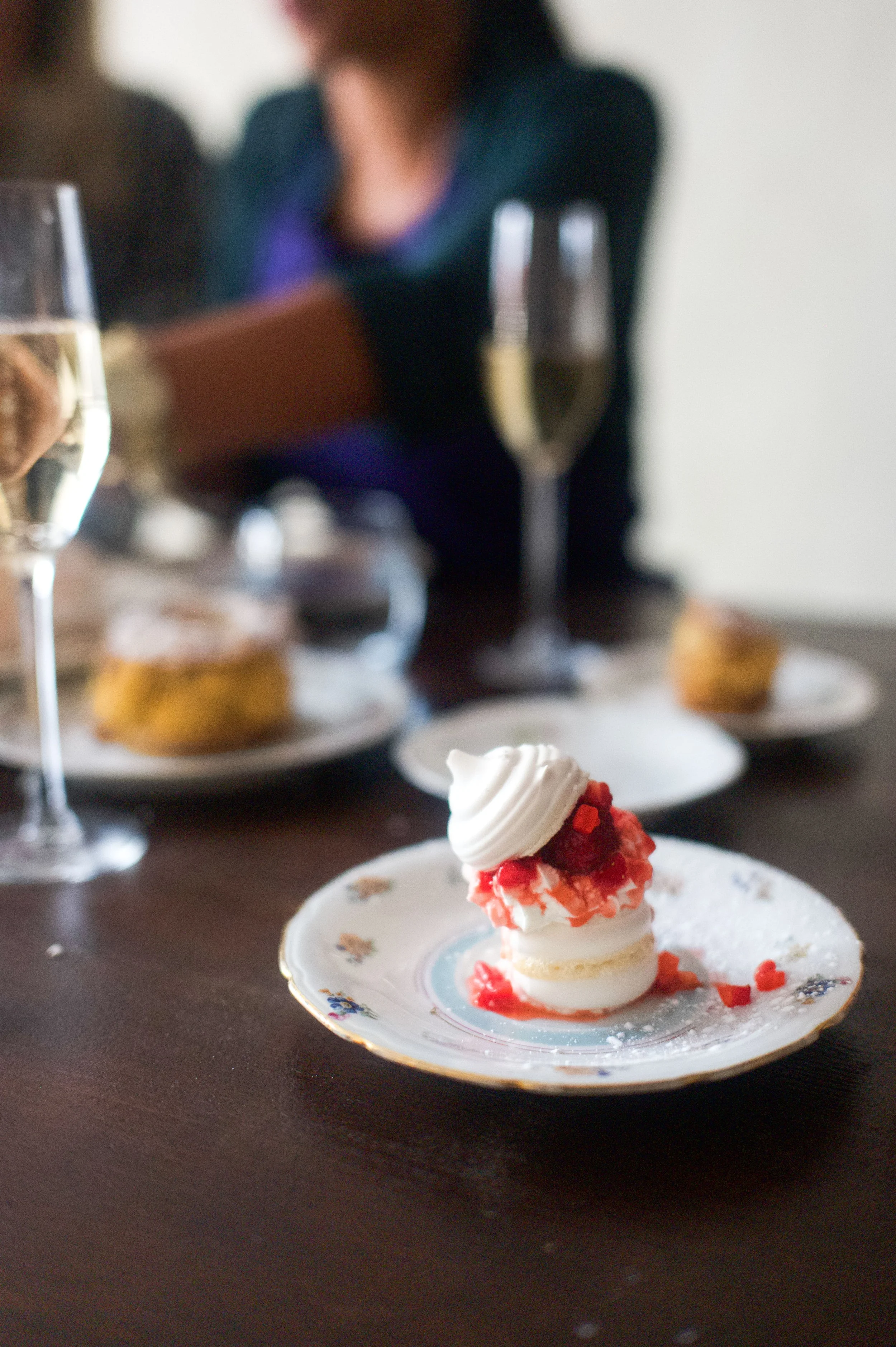 Une petite pâtisserie à la crème avec des morceaux de fruit rouge sur une assiette délicate, avec des verres de champagne et des desserts en arrière-plan lors d'une célébration.