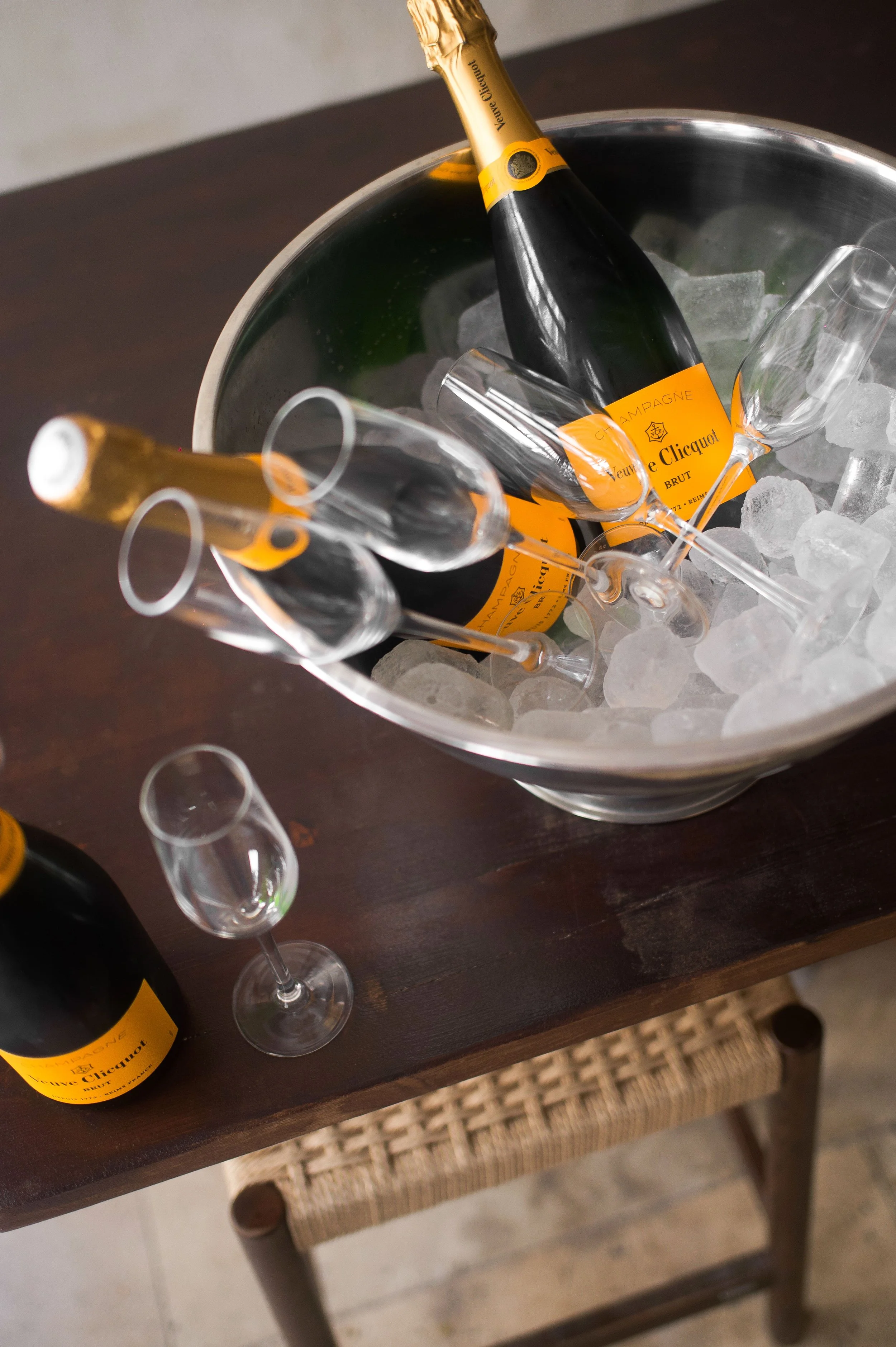 Bouteille de champagne Veuve Clicquot dans un seau à glace avec flûtes à champagne à moitié remplies, sur une table en bois