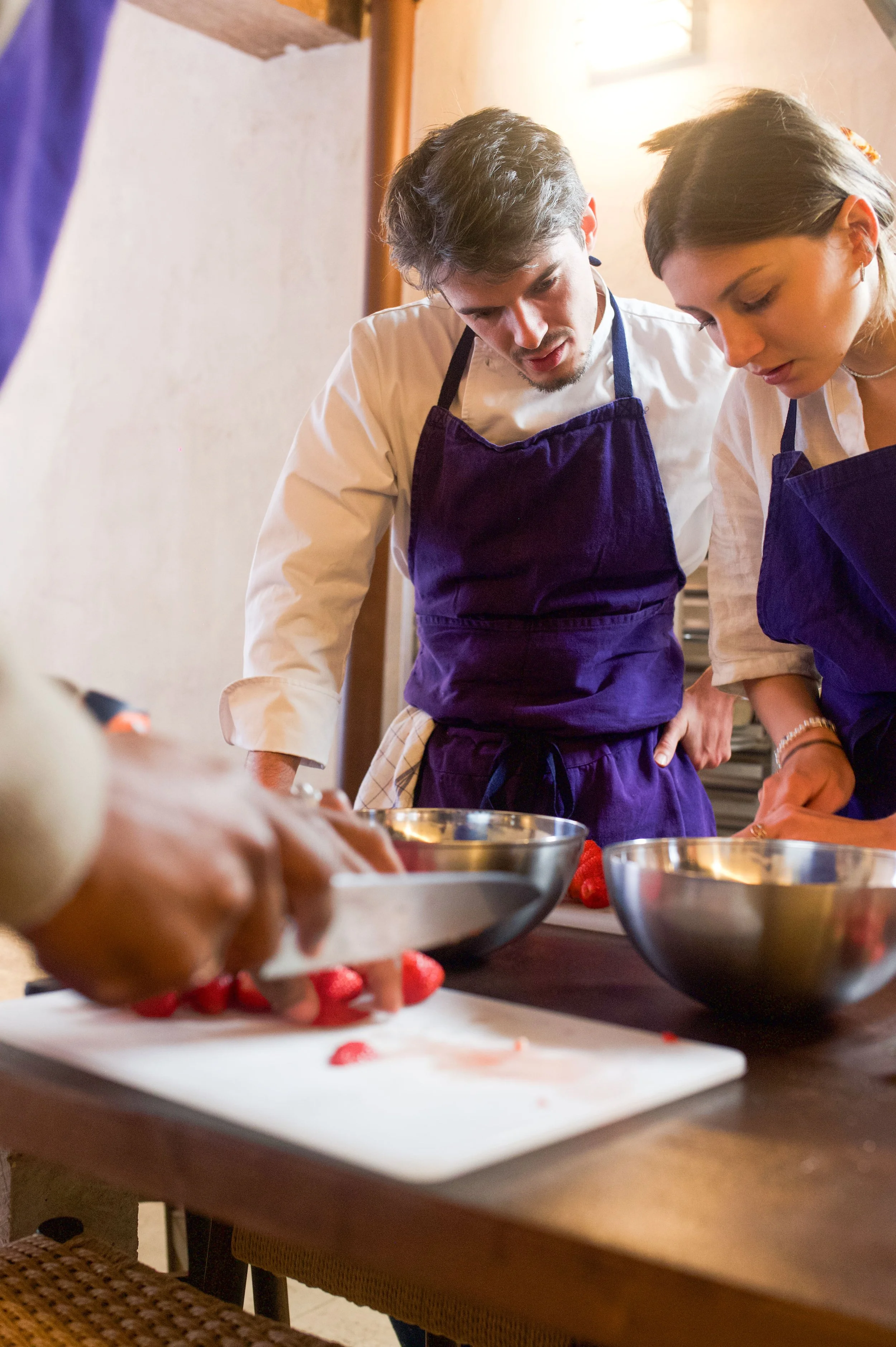 Deux chefs en train de préparer des fraises dans une cuisine, portant des tabliers violets.