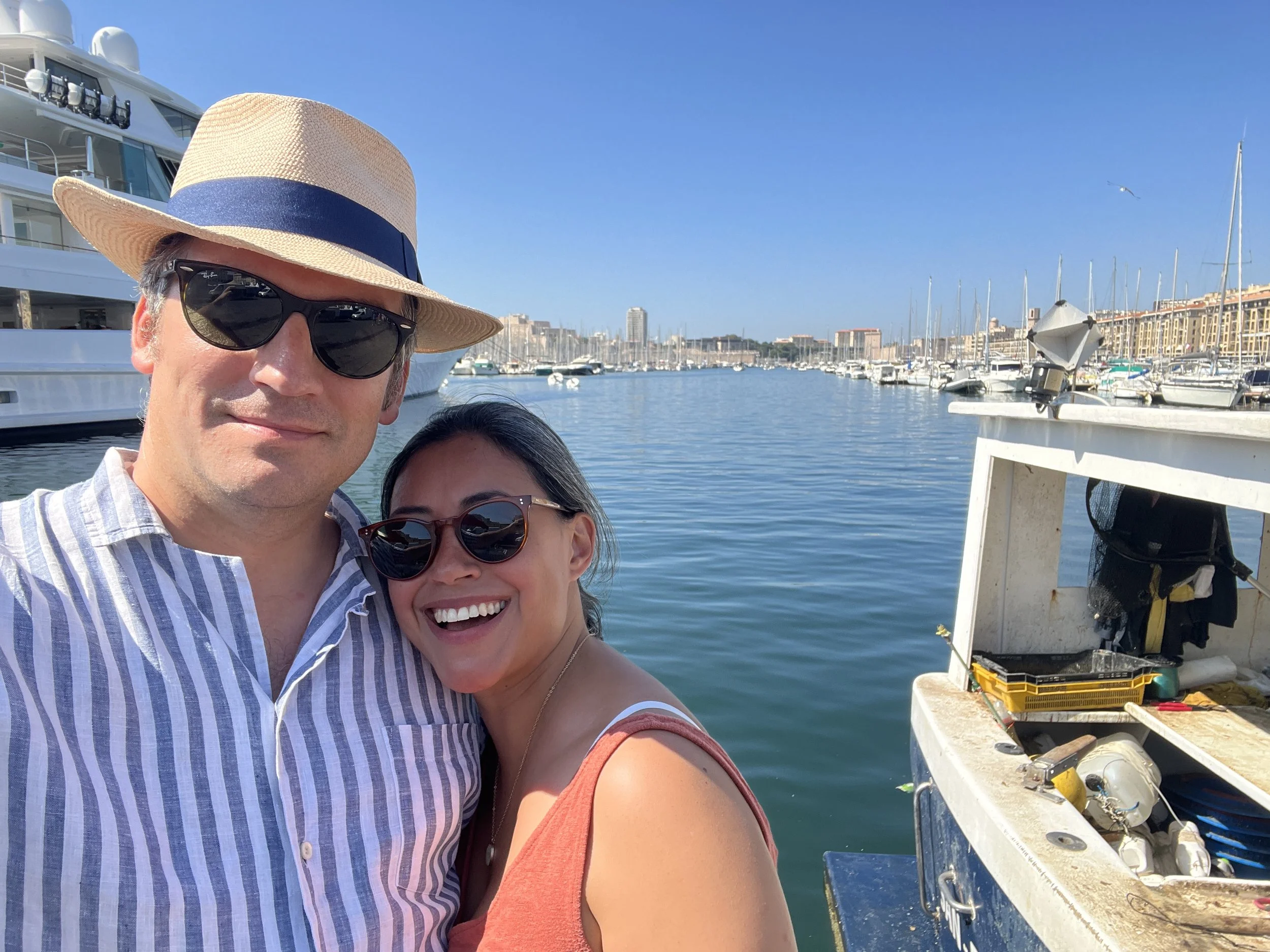 A man and a woman wearing sunglasses standing in front of a marina and water