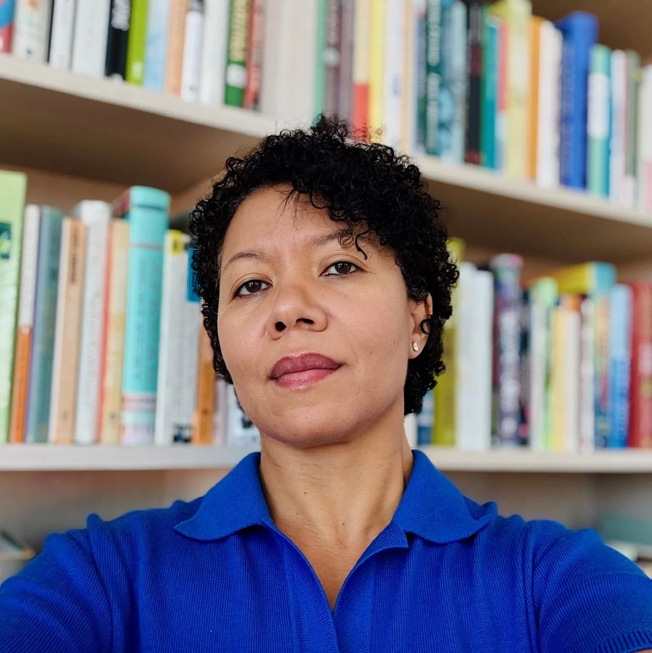 Person with curly dark hair and blue shirt with books in the background
