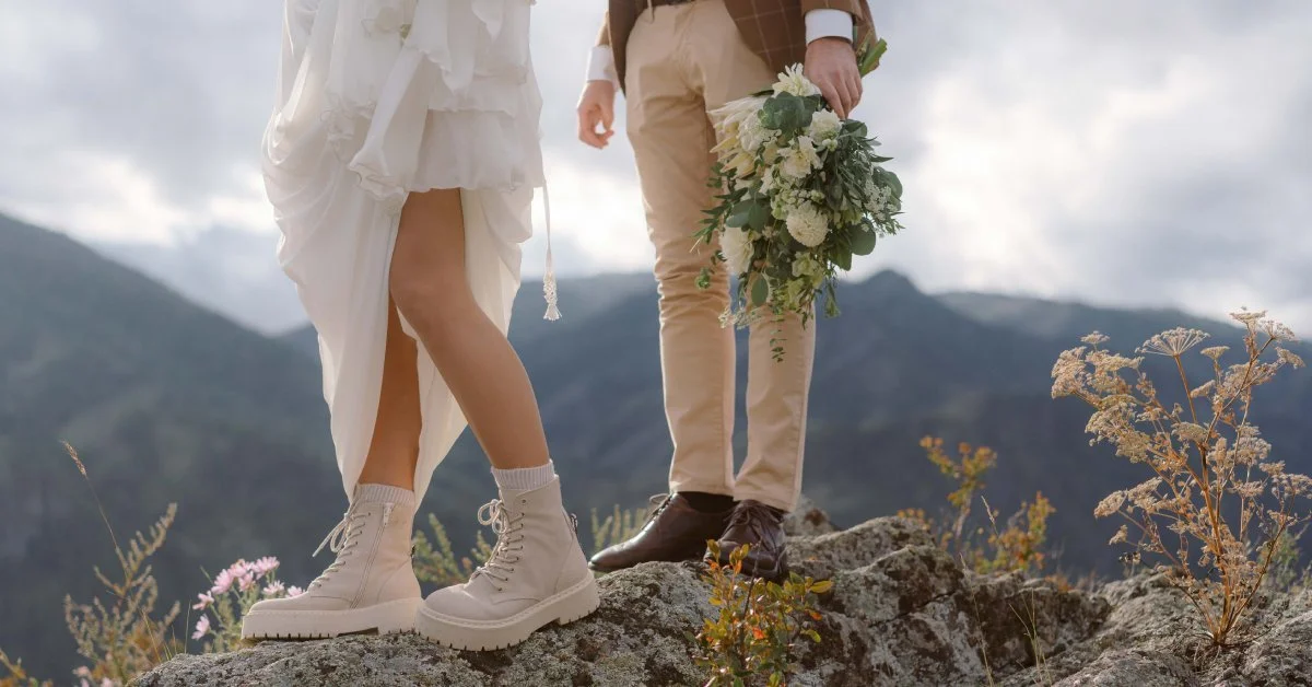 A close-up showing the legs of a bride and groom as they stand together on a large rock in front of a mountain range.