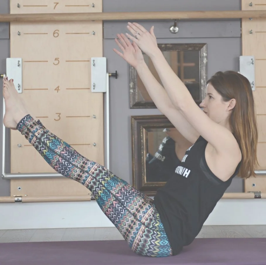 A woman is practicing a pilates move on a yoga mat, emphasizing core stability and control.