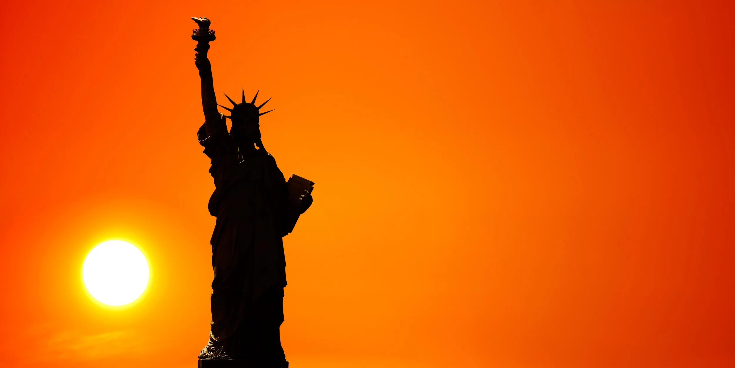 Silhouette of the Statue of Liberty against an orange sunset sky.