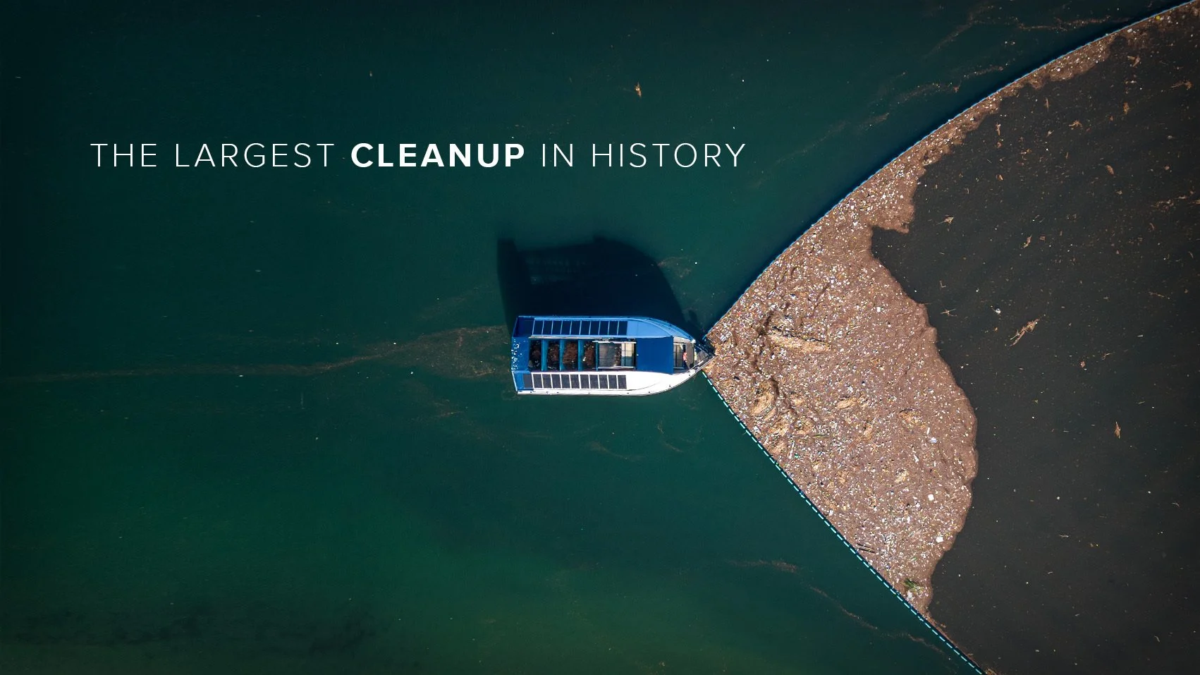 An aerial view of a boat cleaning a polluted water body with a large patch of garbage on the water surface, illustrating the size of a cleanup effort.