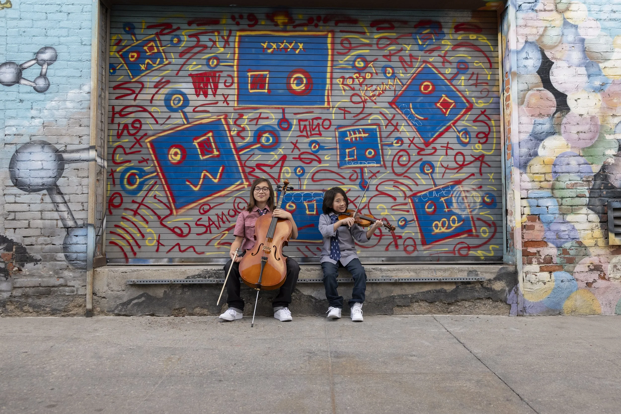 2 boys playing cello + violin in front of a mural