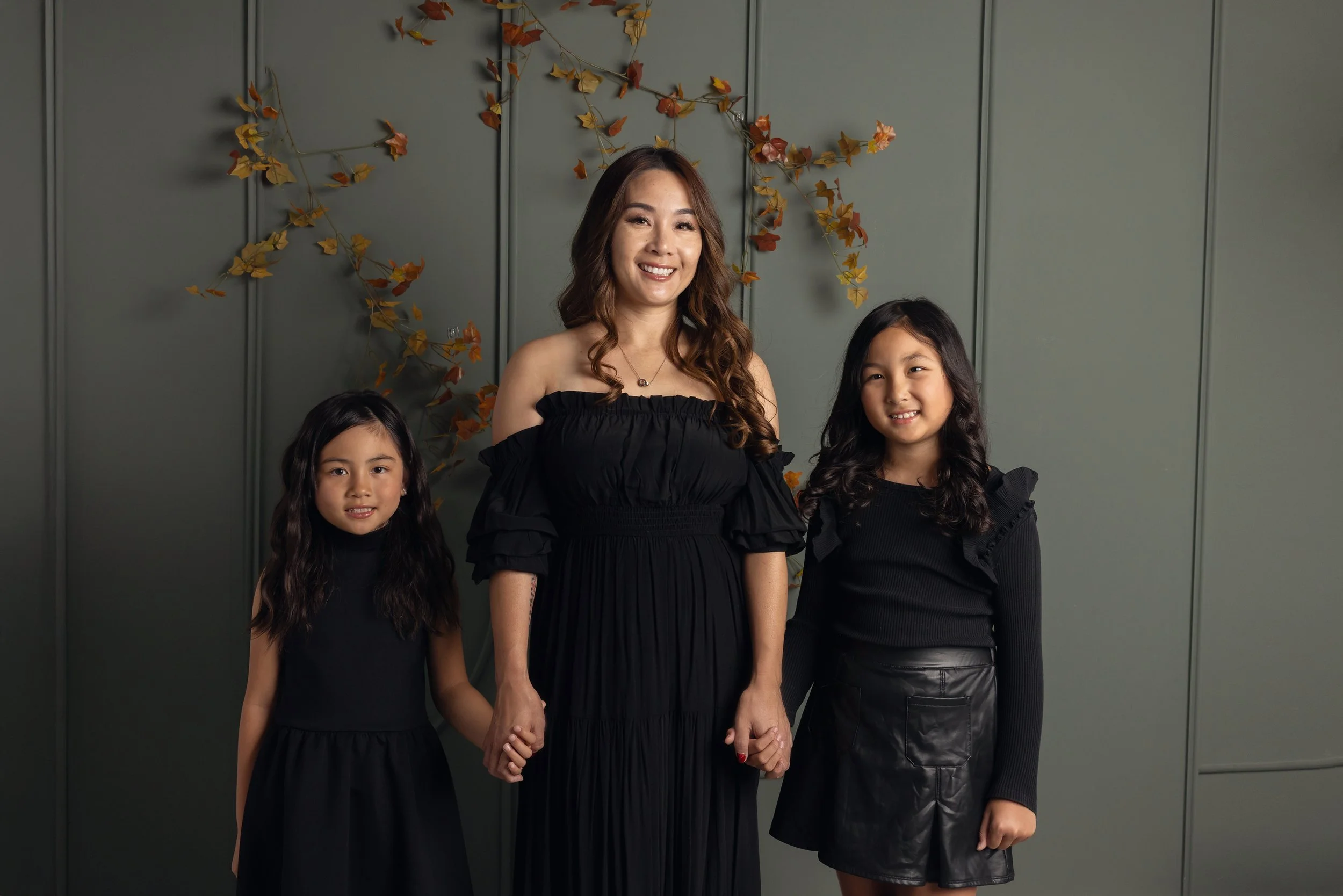 Mom + 2 Daughters in front of a emerald green fall wall